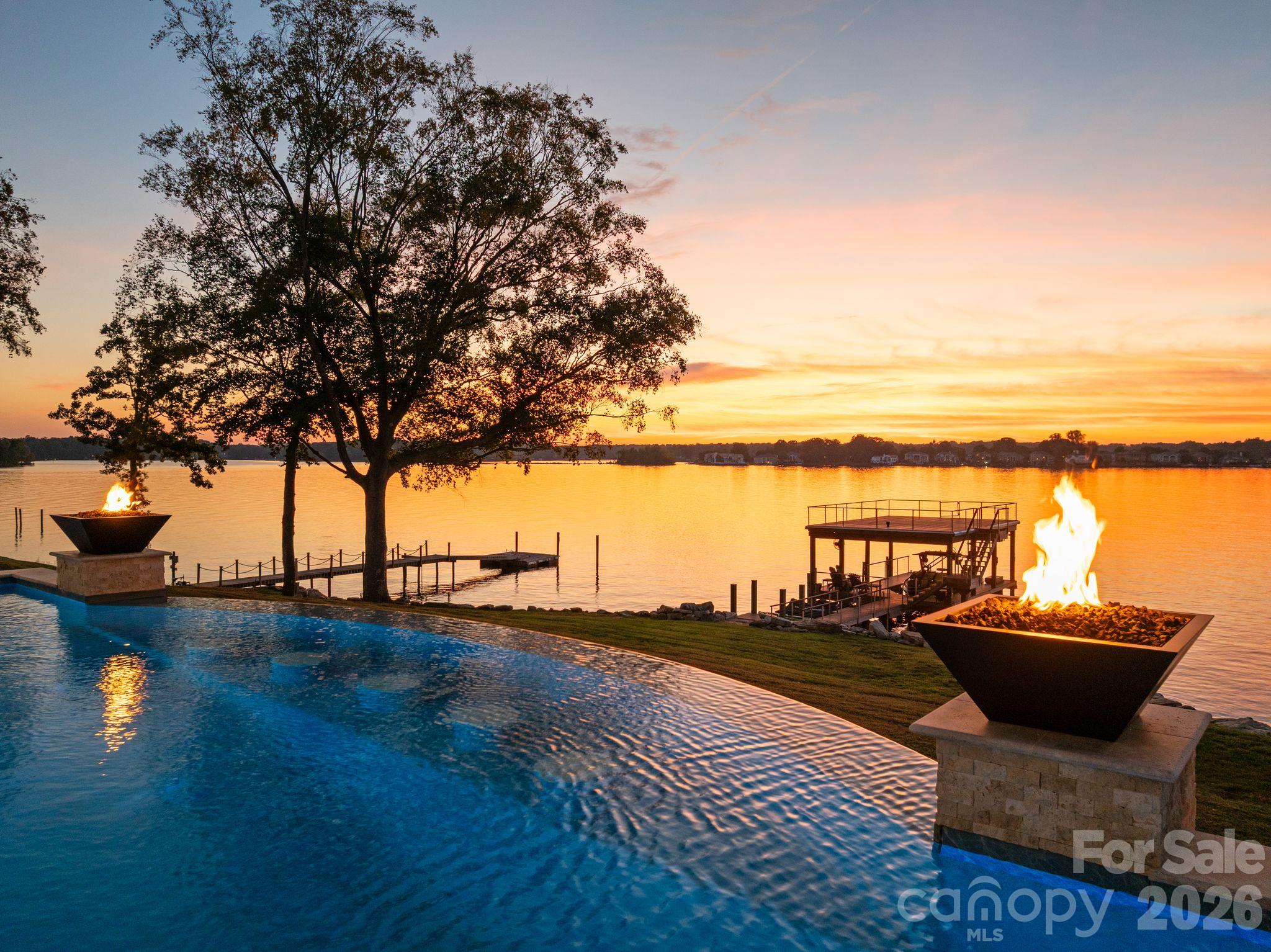 Lakeside pool overlooking the water at sunset, framed by fire bowls and a dock.
