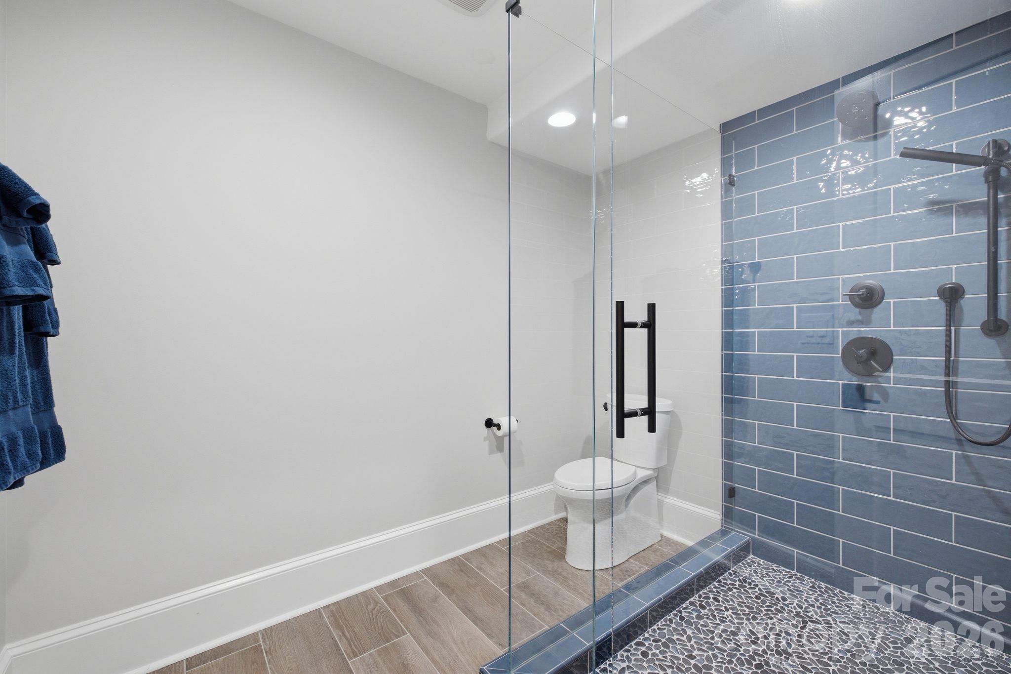 Bathroom with a glass shower, blue subway tile, dark fixtures, and pebble-tile flooring.