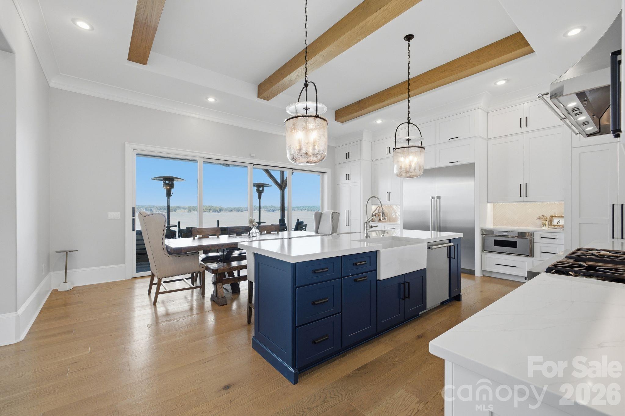 Modern kitchen with a navy island, wood ceiling beams, and large windows overlooking the water.