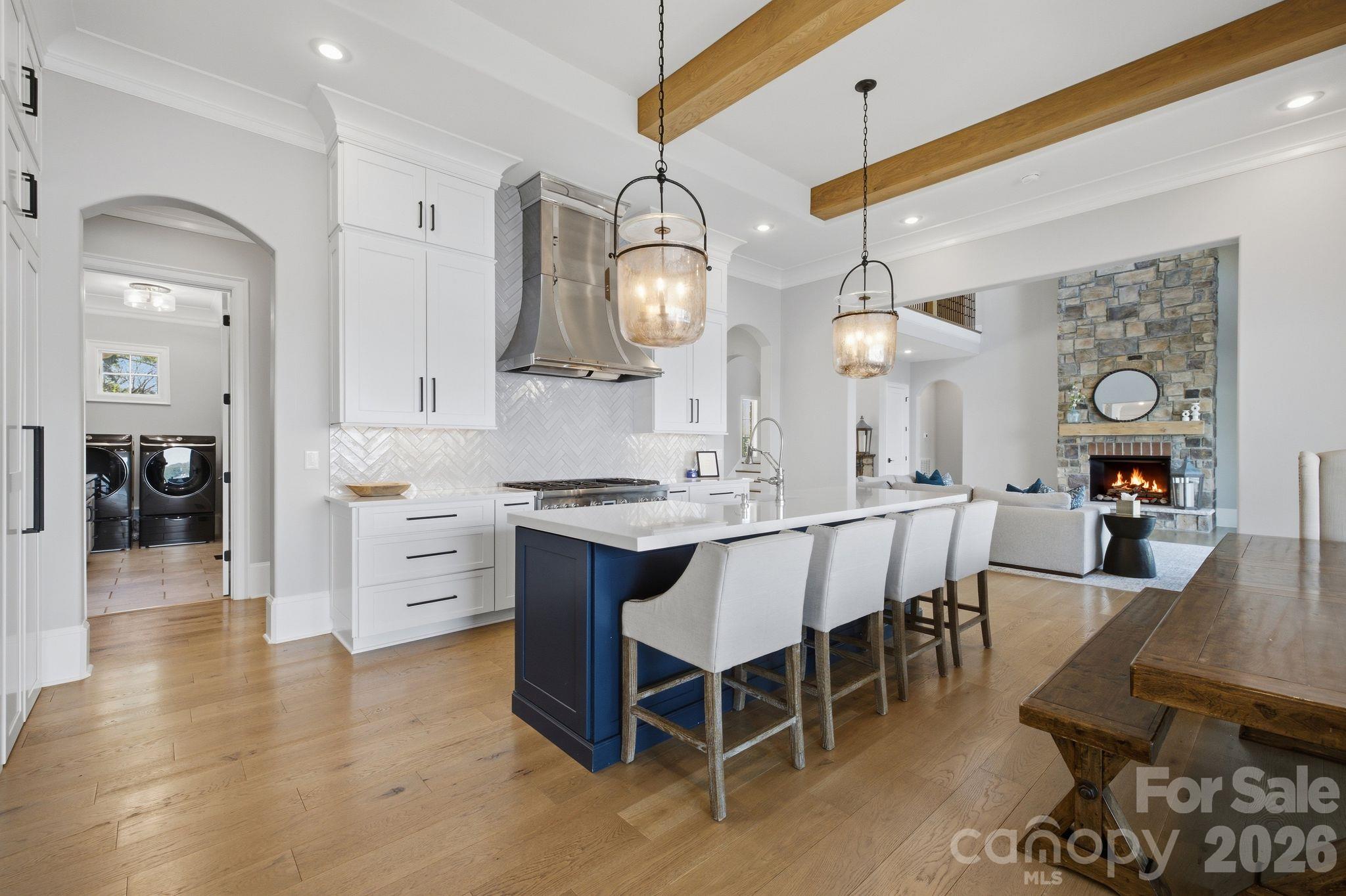 Open-plan kitchen with navy island, white stools, wood ceiling beams, and stone fireplace.