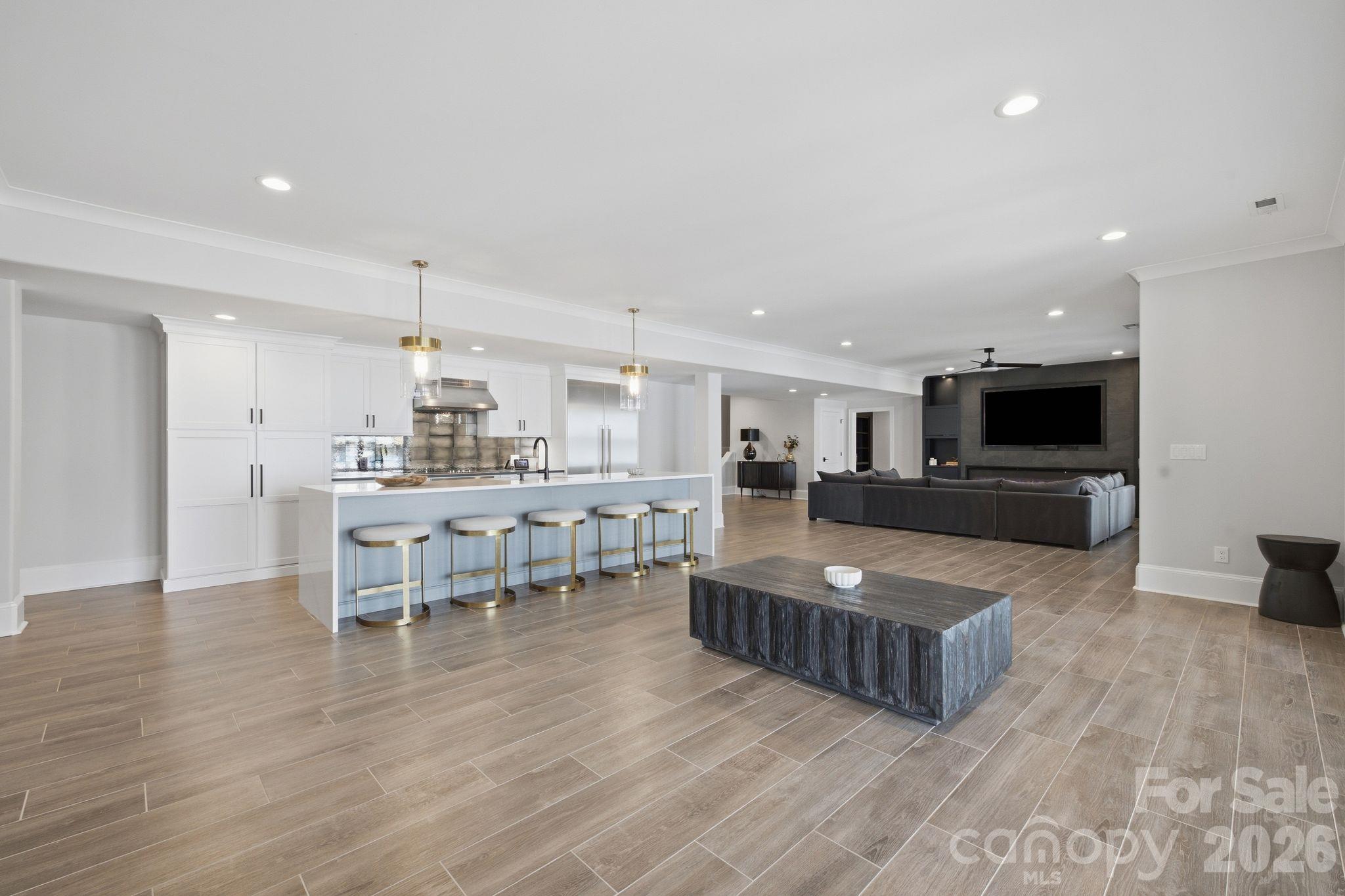 Open-plan kitchen and living room with a five-stool island and dark media wall.