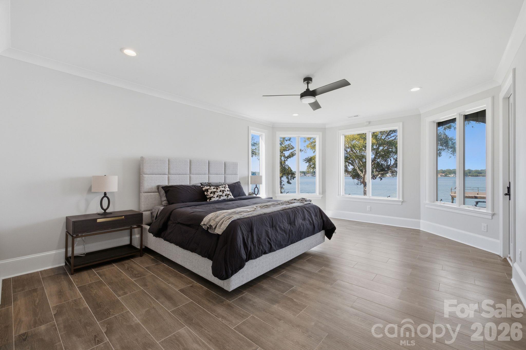 Furnished bedroom with dark bedding and wide windows overlooking the lake.