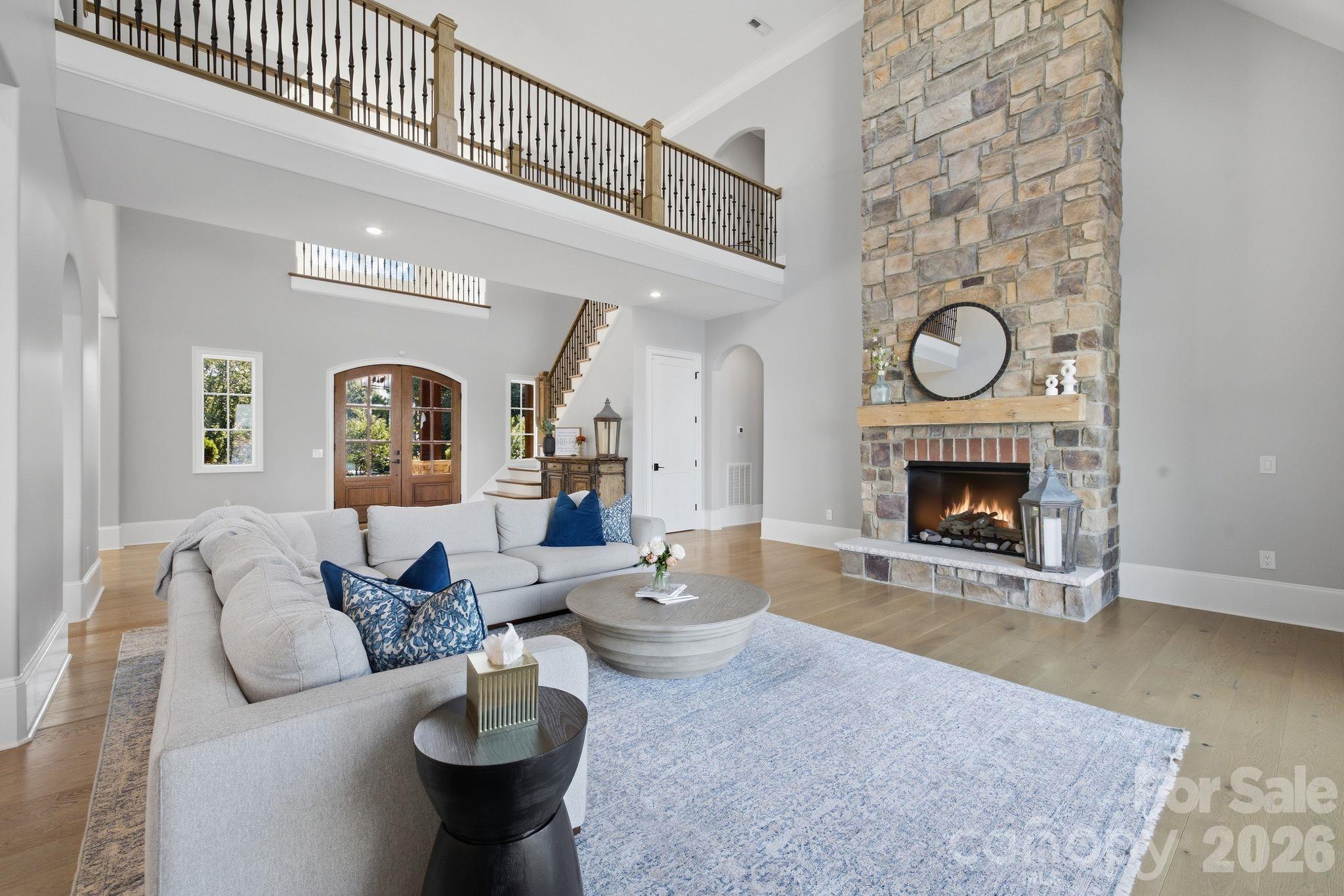 Two-story living room with a tall stone fireplace, open gallery, and gray sectional.