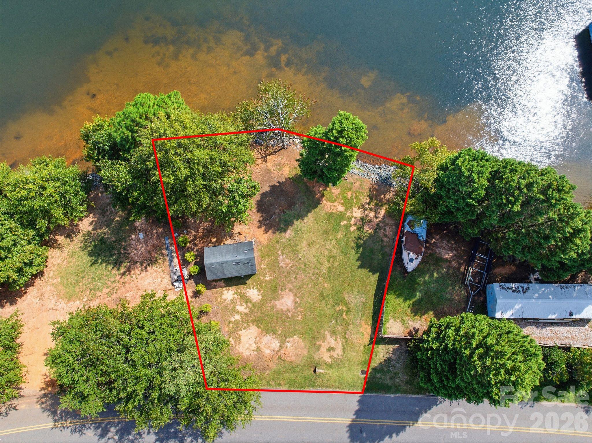 Aerial view of a red-outlined, wooded lakeside lot beside a road.