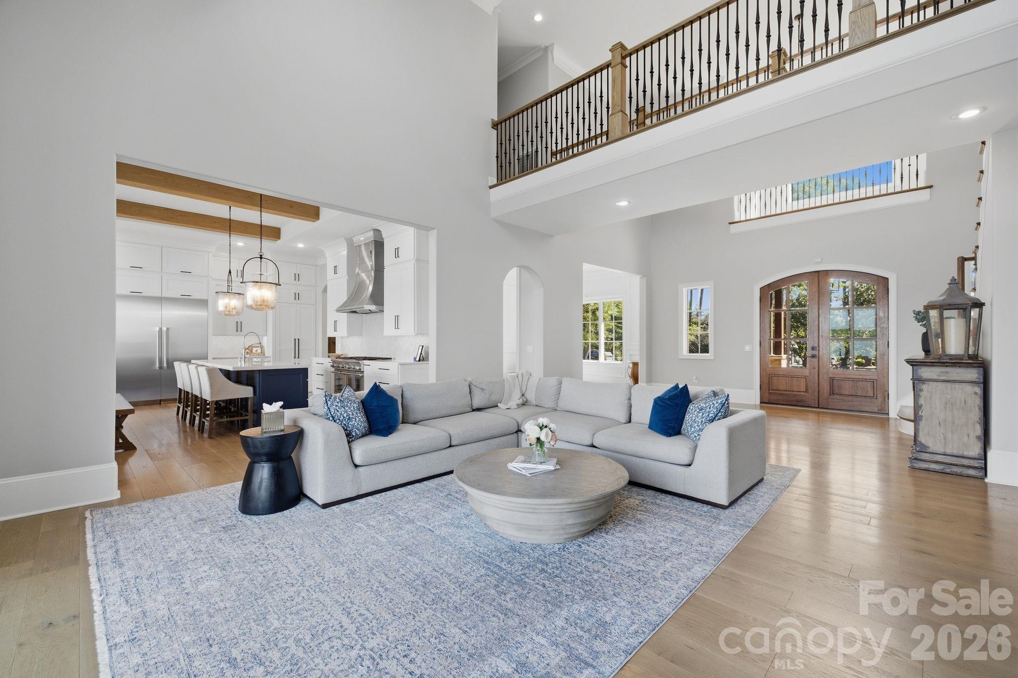 Furnished open-plan living room with gray sectional, navy kitchen island, vaulted ceiling, and arched wood doors.