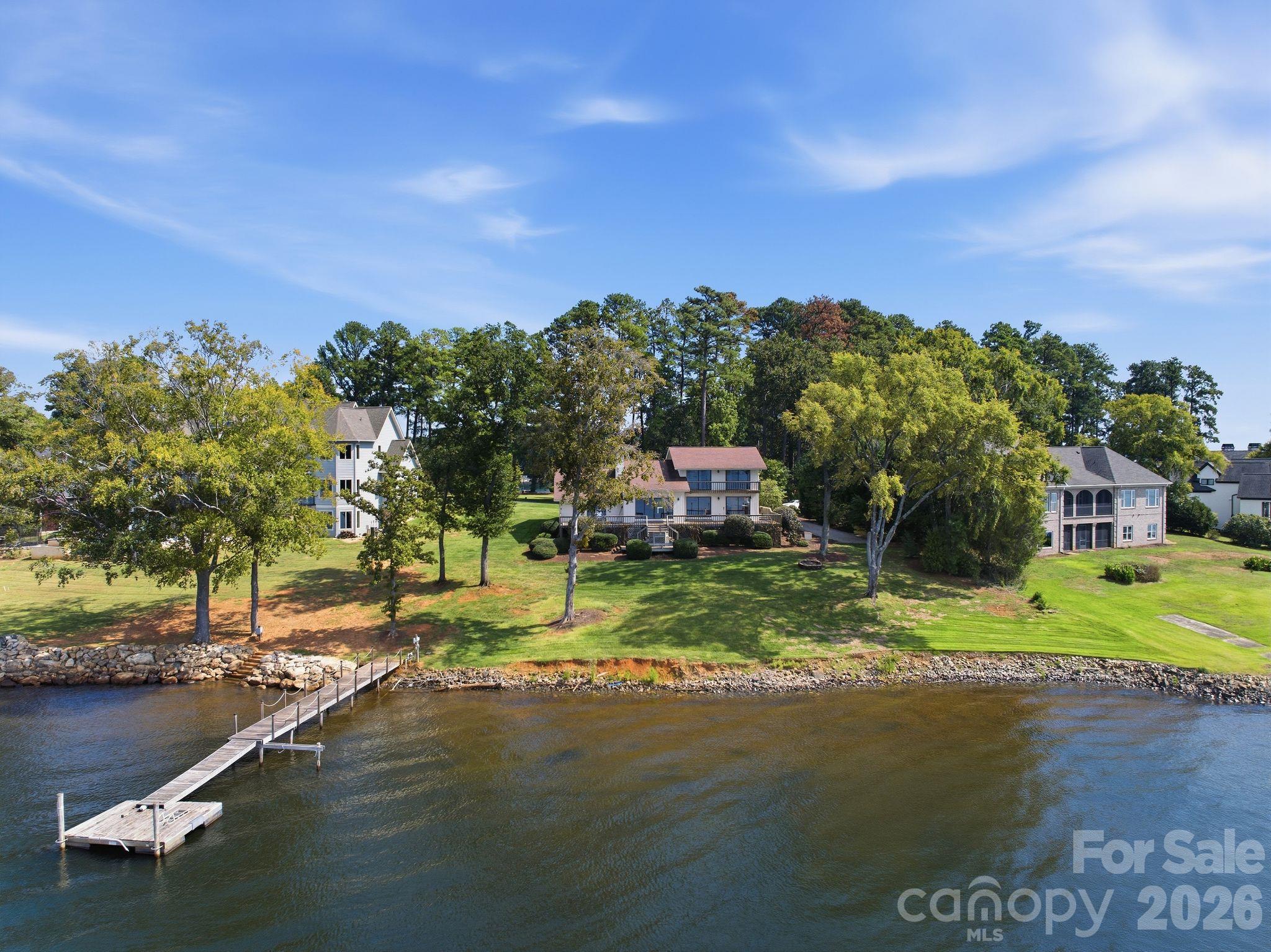 Aerial view of waterfront homes, lawns, and a long dock extending into the lake.
