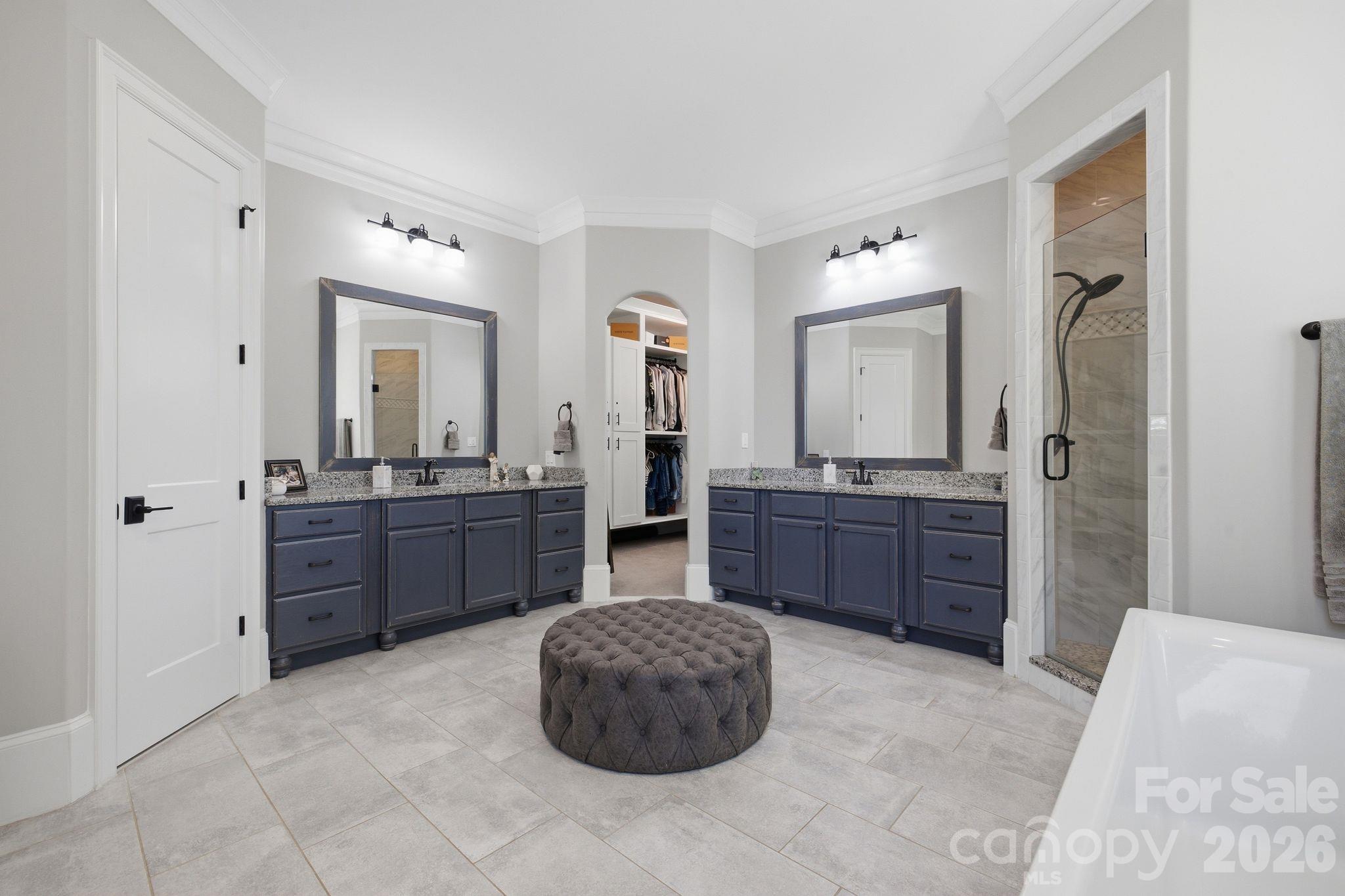 Spacious bathroom with dual dark blue vanities, a central walk-in closet, and a glass-enclosed shower.