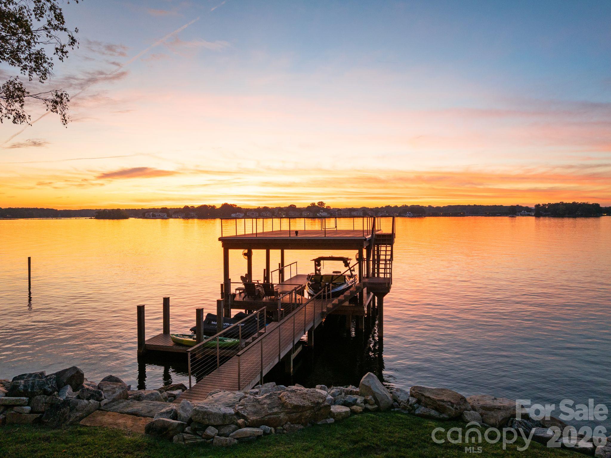 Covered lake dock with boats silhouetted against a vivid sunset.