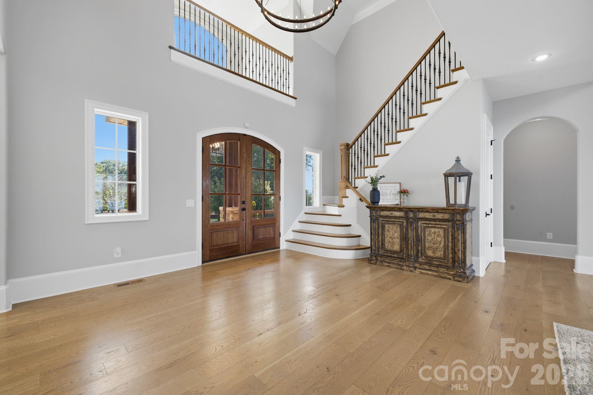 Foyer with arched wood entry door, curved staircase, oak floors, and water visible through a window.