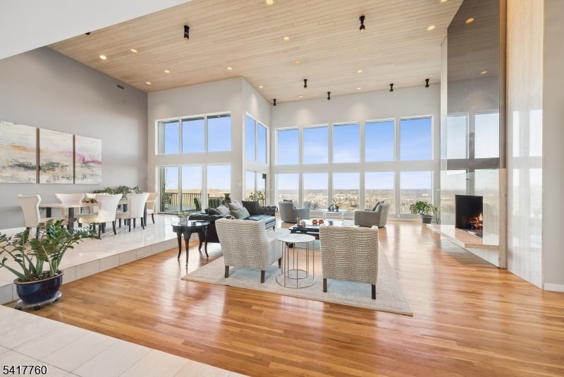 Furnished great room with a high wood ceiling, tall windows, hardwood floors, and a fireplace.