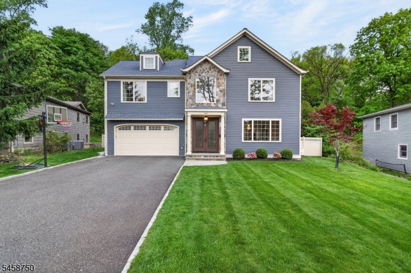 Two-story gray house with stone entry accents, attached garage, paved driveway, and green lawn.