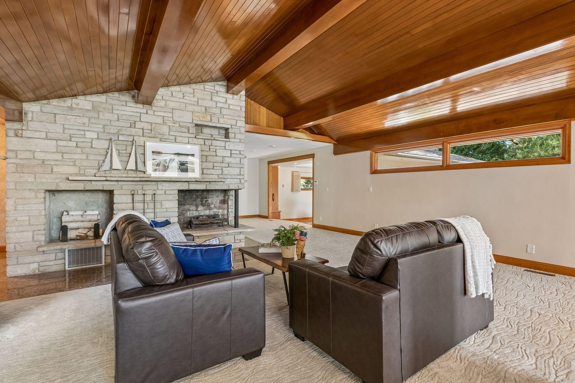 Living room with a vaulted wood ceiling, stone fireplace, and dark leather sofas.