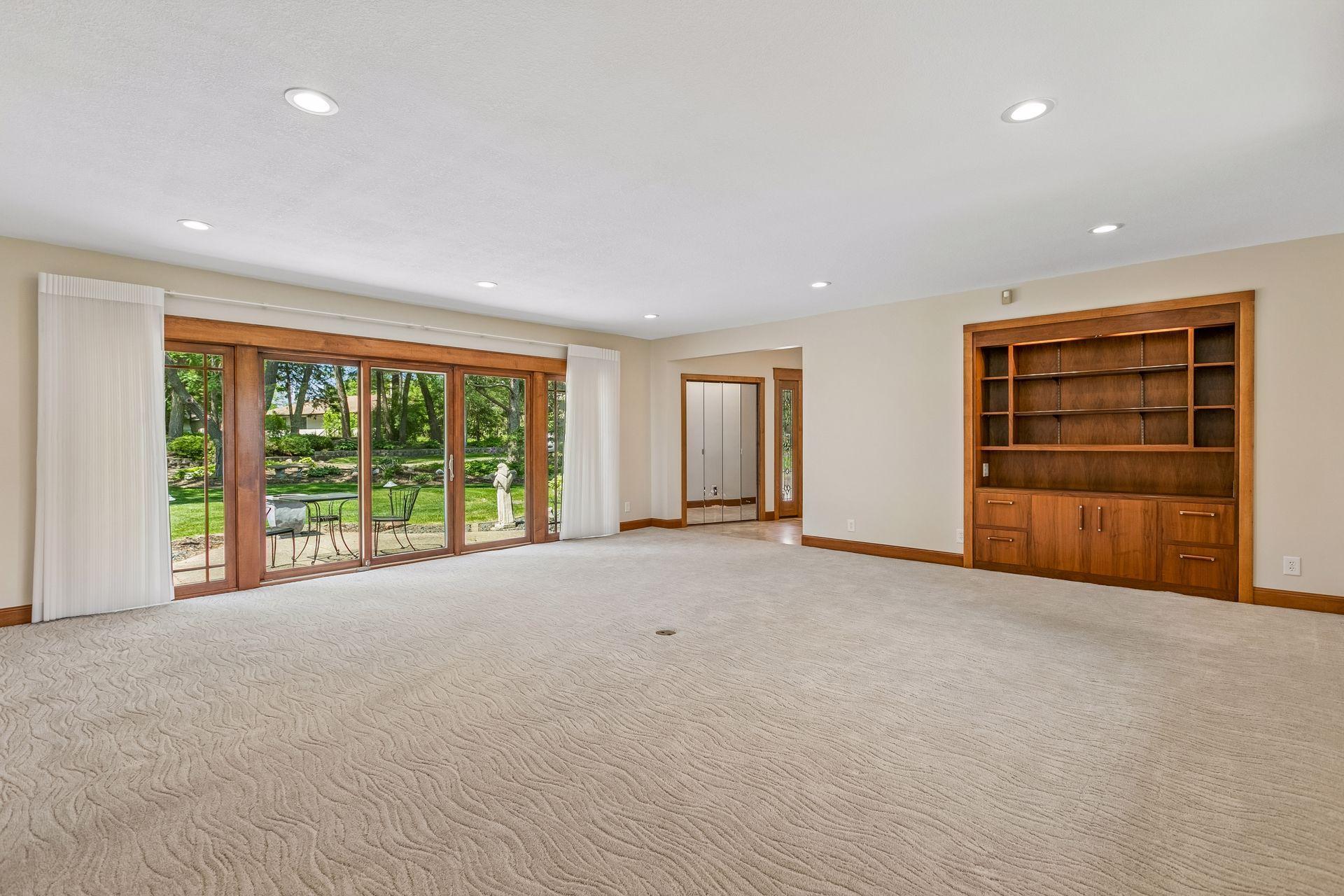 Vacant living room with built-in wooden shelving and sliding glass doors overlooking a garden.