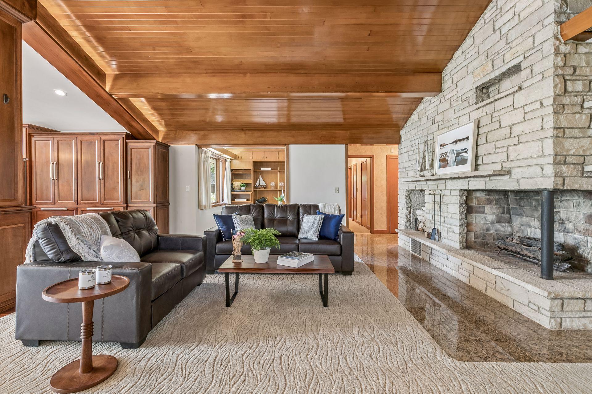 Living room with a white stone fireplace, leather sofas, and a warm wood-paneled ceiling.