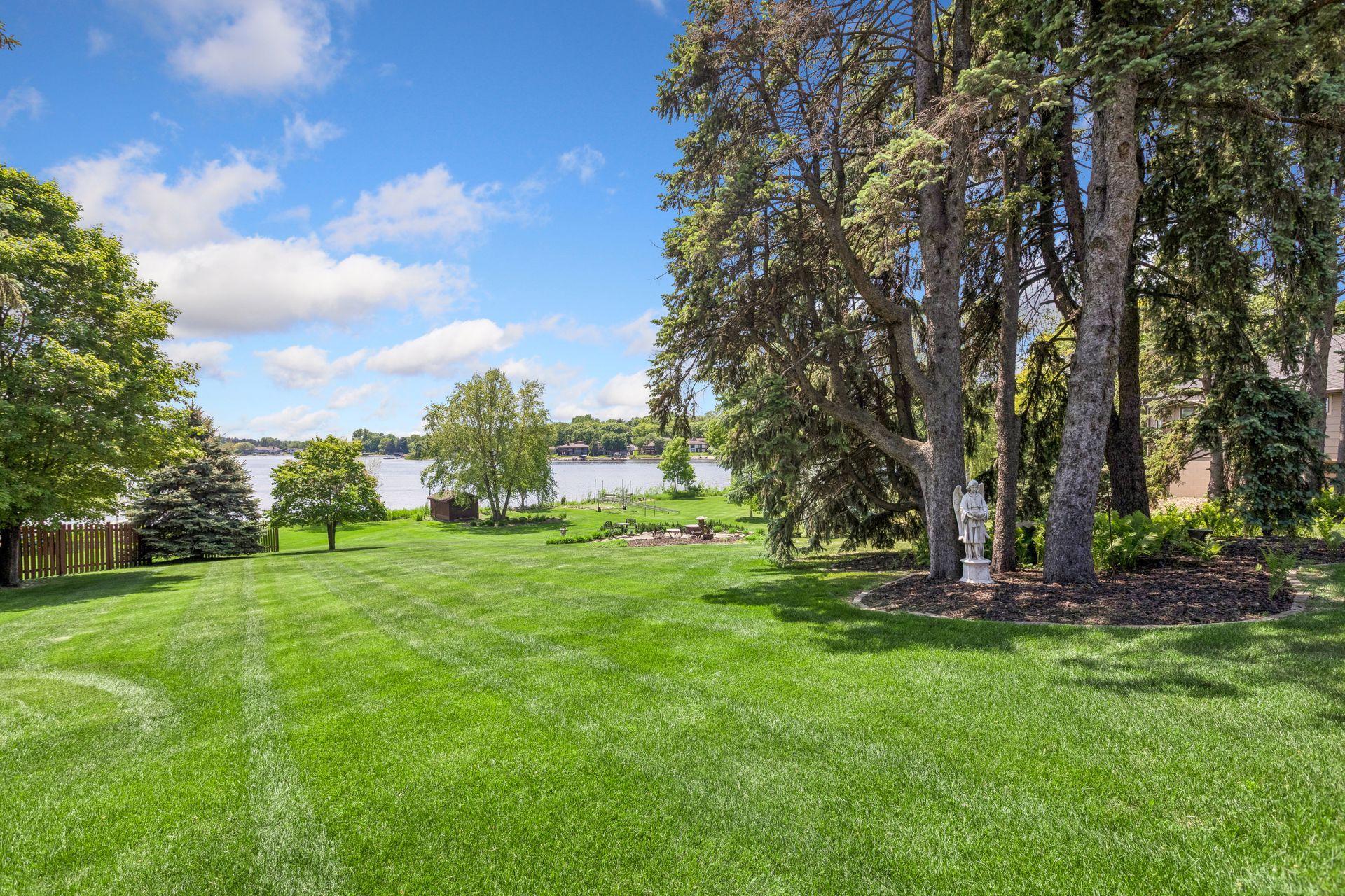 Lakeside lawn with mature trees, a garden statue, and seating near the water.