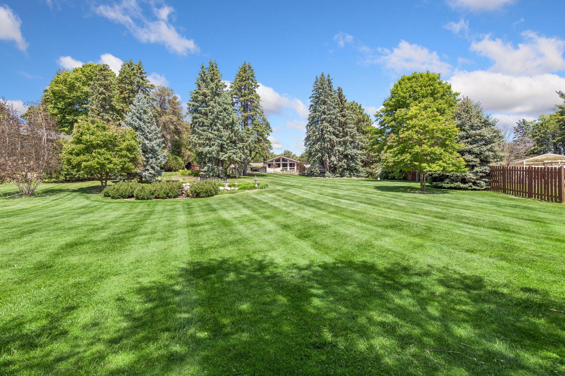 Spacious green lawn leading to a house among mature trees and landscaped garden beds.