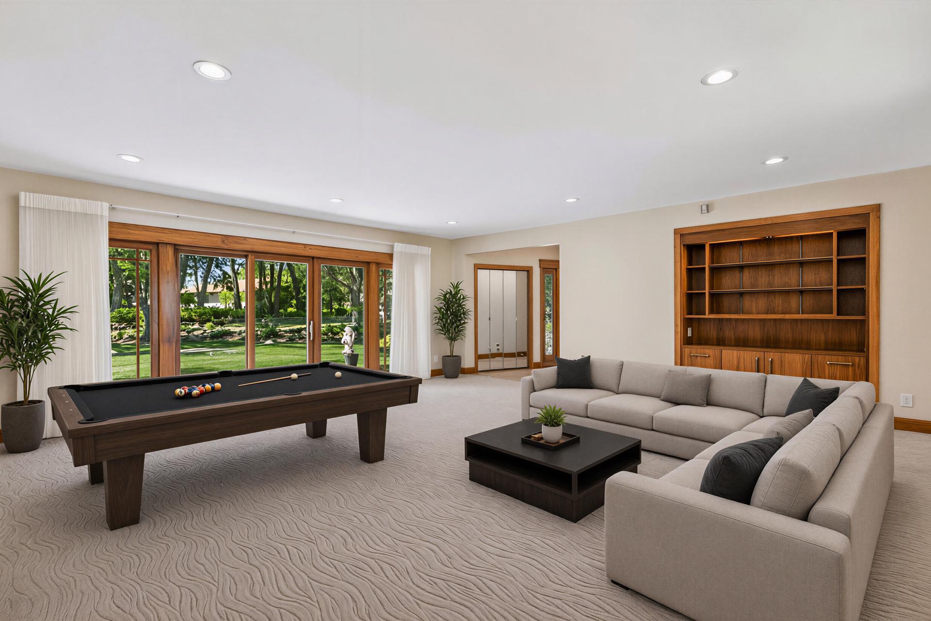 Billiard room with a pool table, sectional sofa, and large windows overlooking a garden.