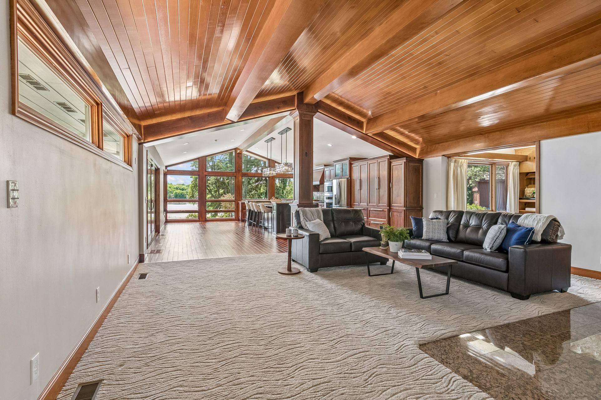 Living room with a vaulted wood ceiling, leather sofas, and large windows overlooking the water.