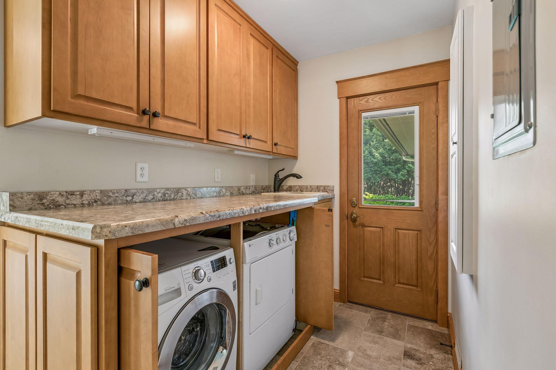Laundry room with washer, dryer, wood cabinetry, and a windowed exterior door.