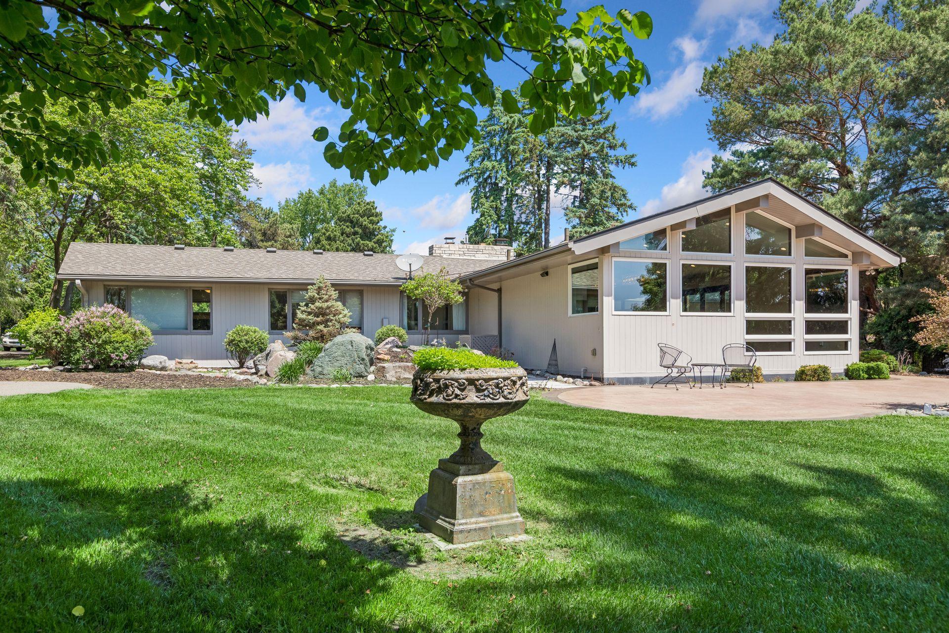 Contemporary home with tall front windows, landscaped lawn, mature trees, and a stone fountain.
