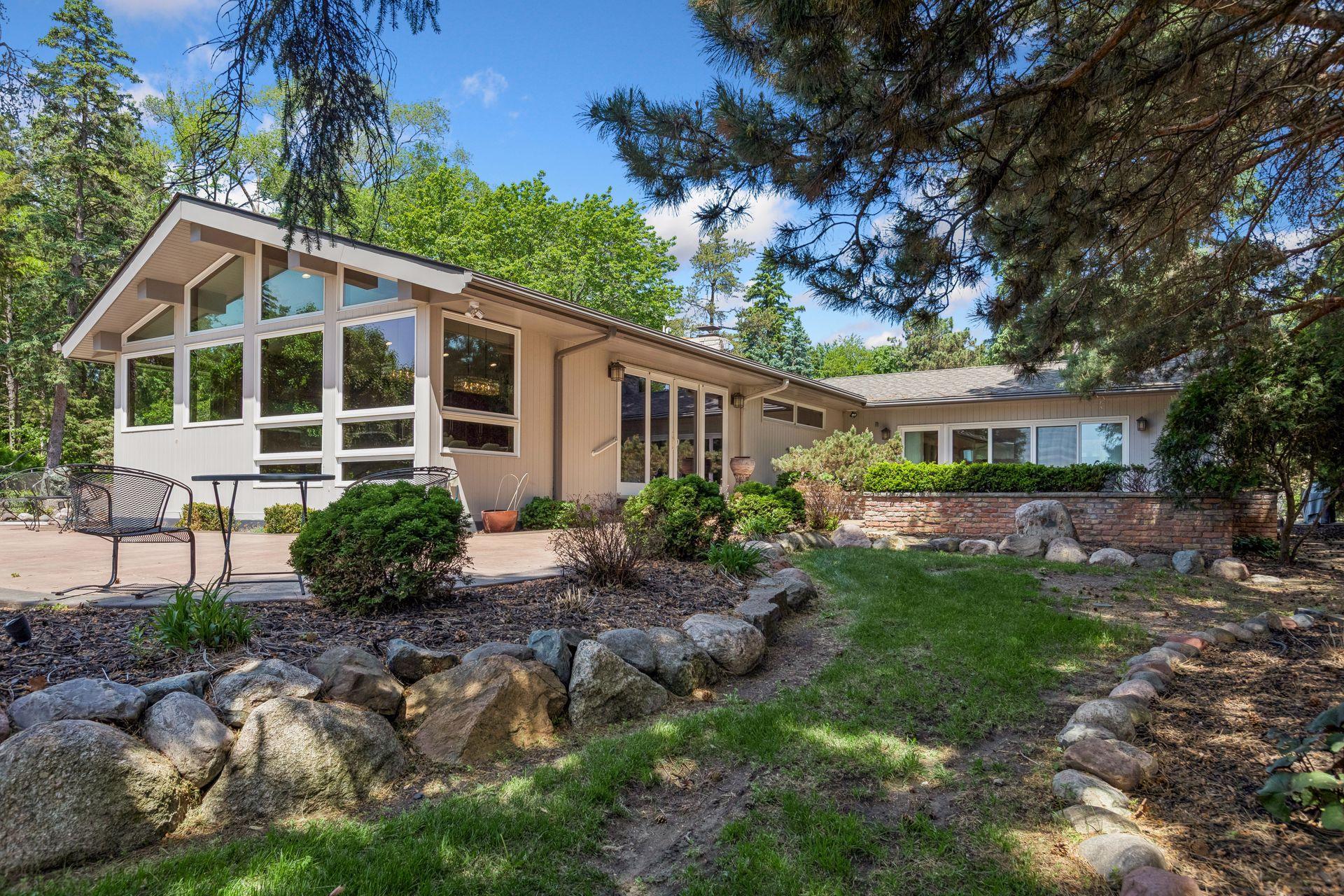 Home with a glass-front gable, patio seating, and landscaped grounds beneath mature trees.