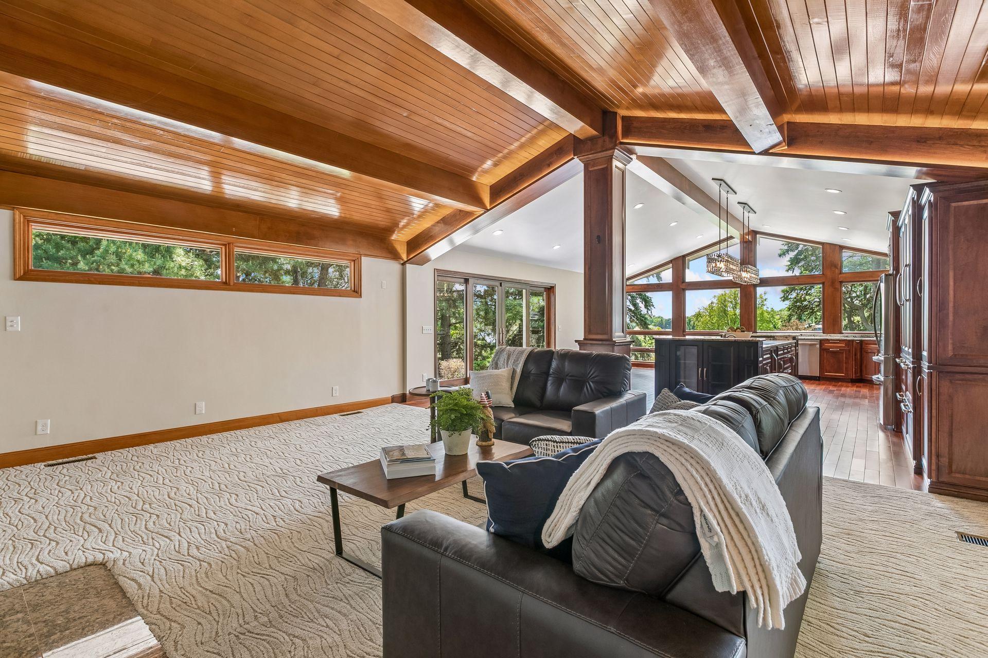 Living room with vaulted wood ceiling, leather sofas, and large windows beside the kitchen.