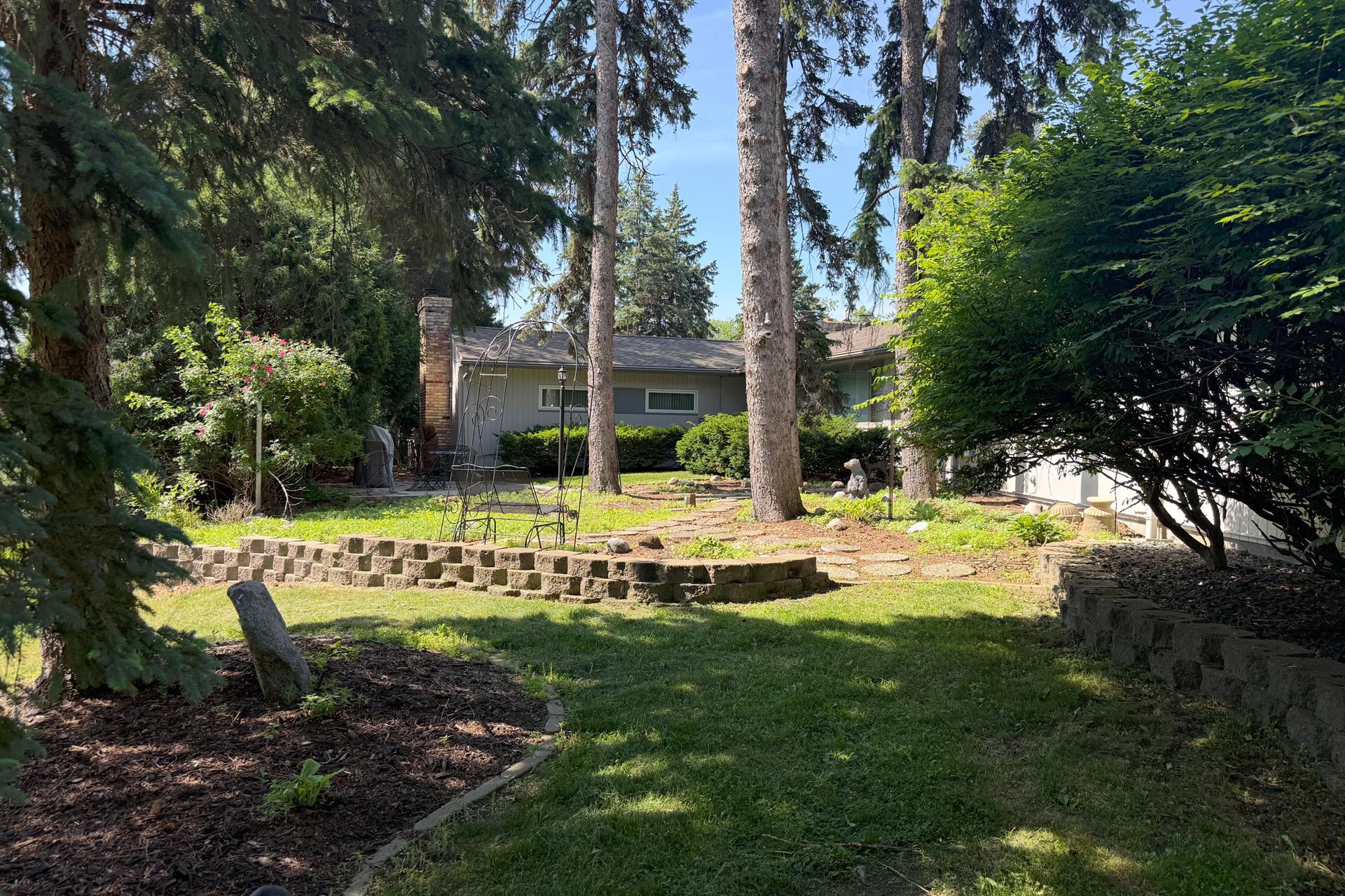 Backyard with mature trees, stone retaining walls, landscaped beds, and a metal garden swing.