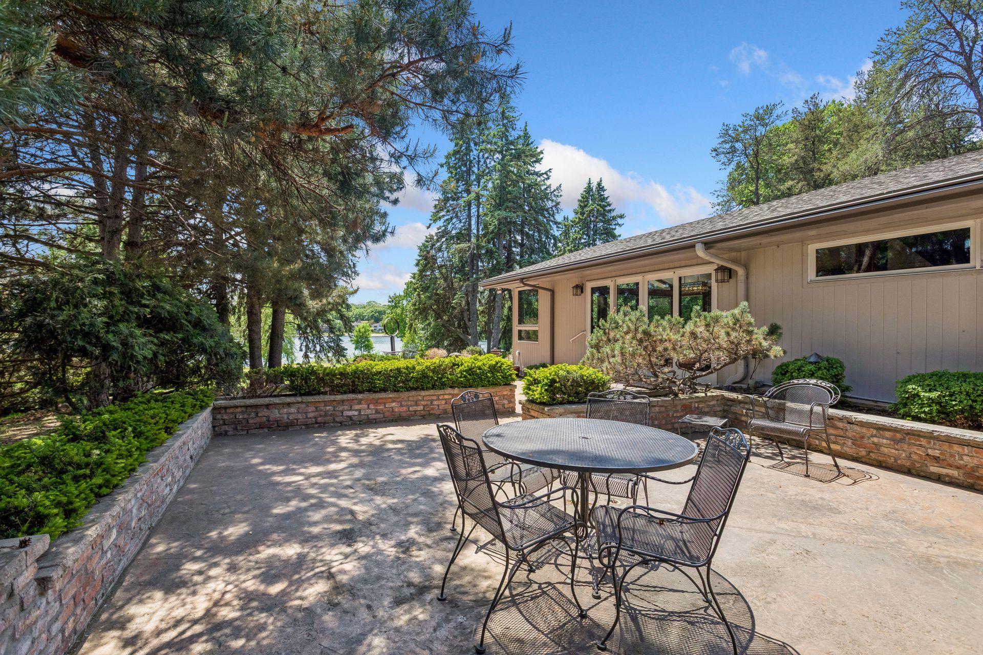 Lakeside patio with a round metal dining table, brick planters, and mature trees.
