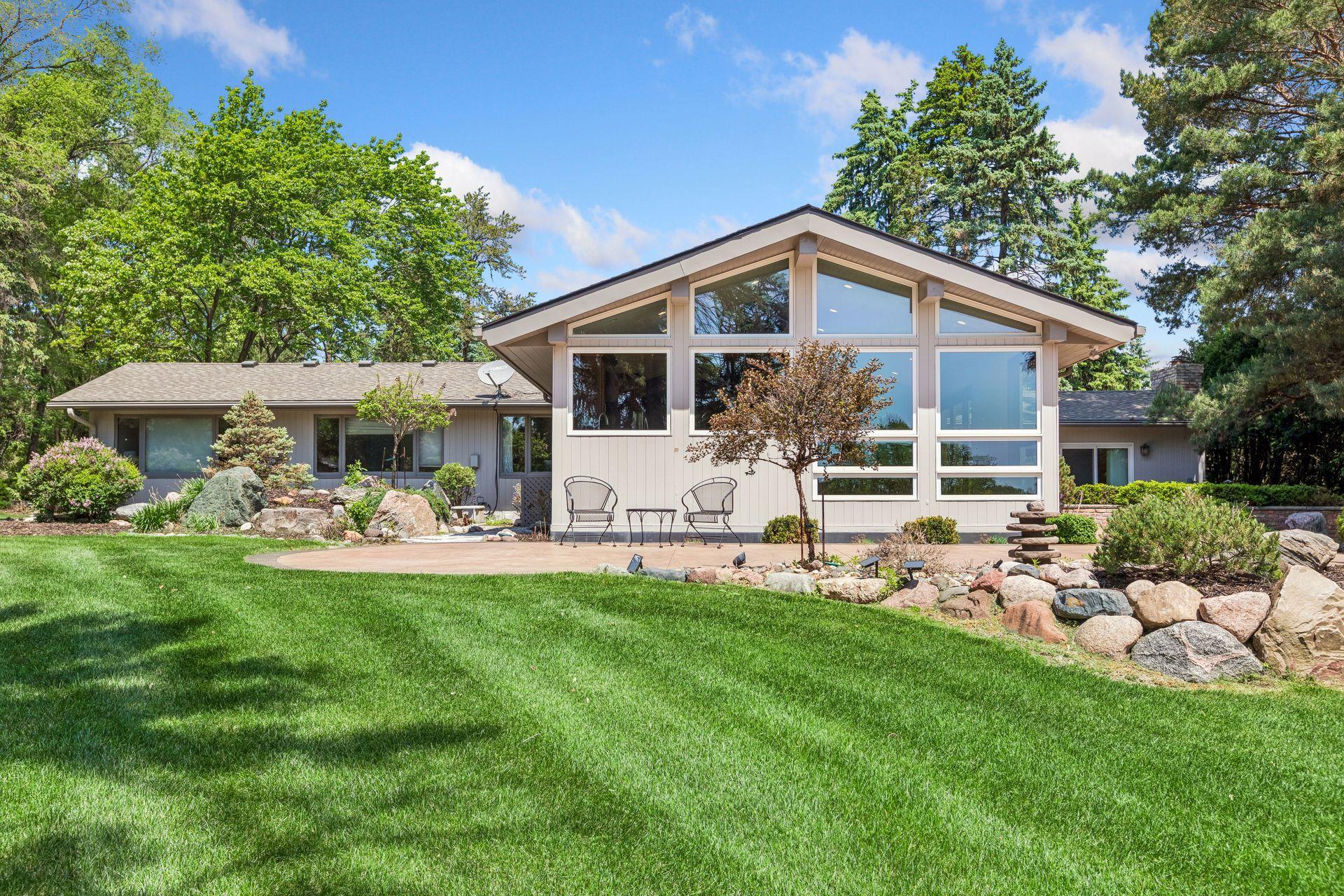 Home with a tall gabled window facade, landscaped rock garden, and patio chairs.