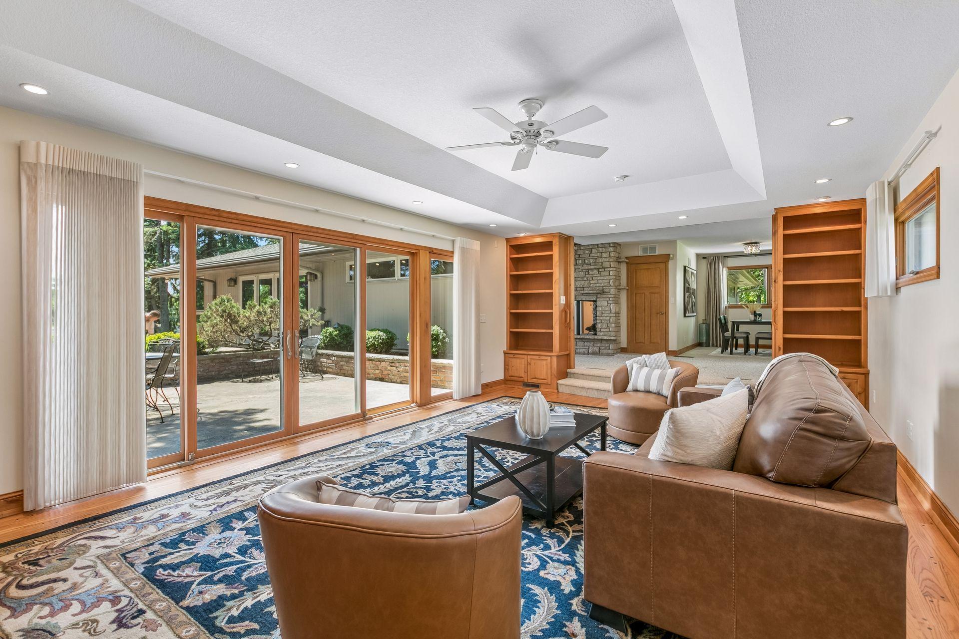 Living room with leather seating, built-in bookshelves, stone fireplace, and sliding glass doors to a patio.