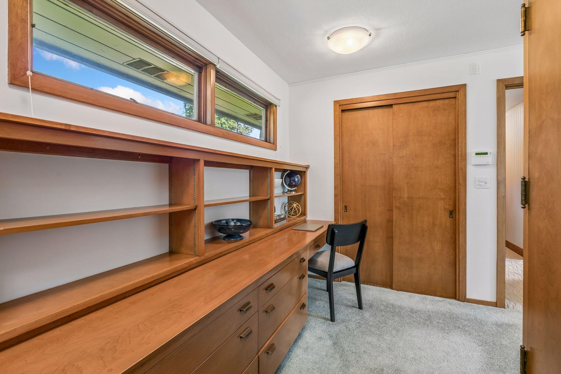 Home office with built-in wooden desk and shelves beneath high windows.