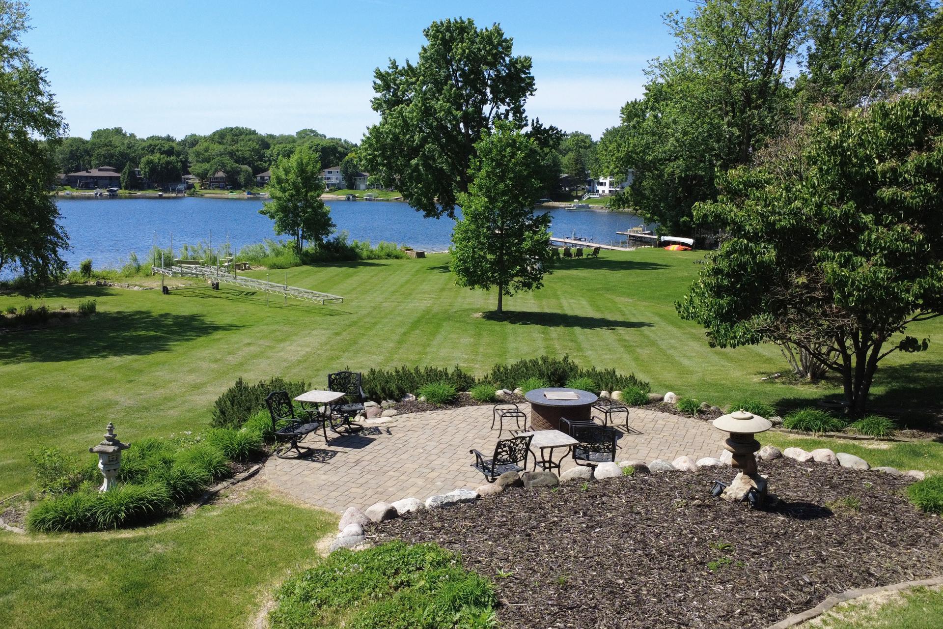 Lakefront yard with a broad lawn, brick patio seating, and a dock beside the water.