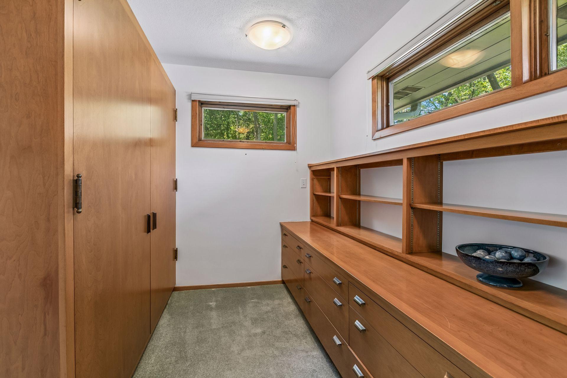 Storage room with extensive wood cabinetry, built-in shelving, and two high windows.