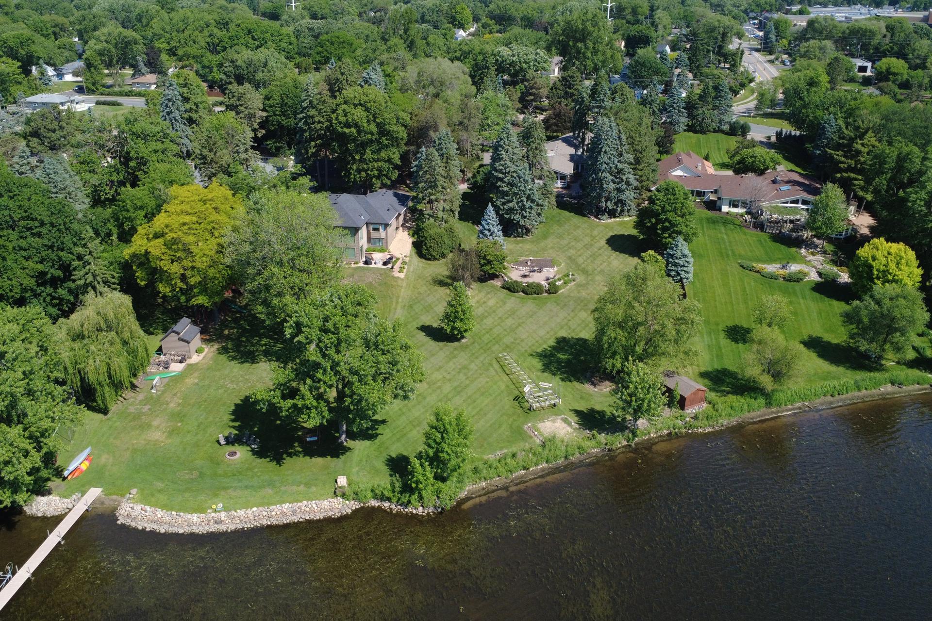 Aerial view of a lakeside home with a broad lawn, mature trees, and a dock.