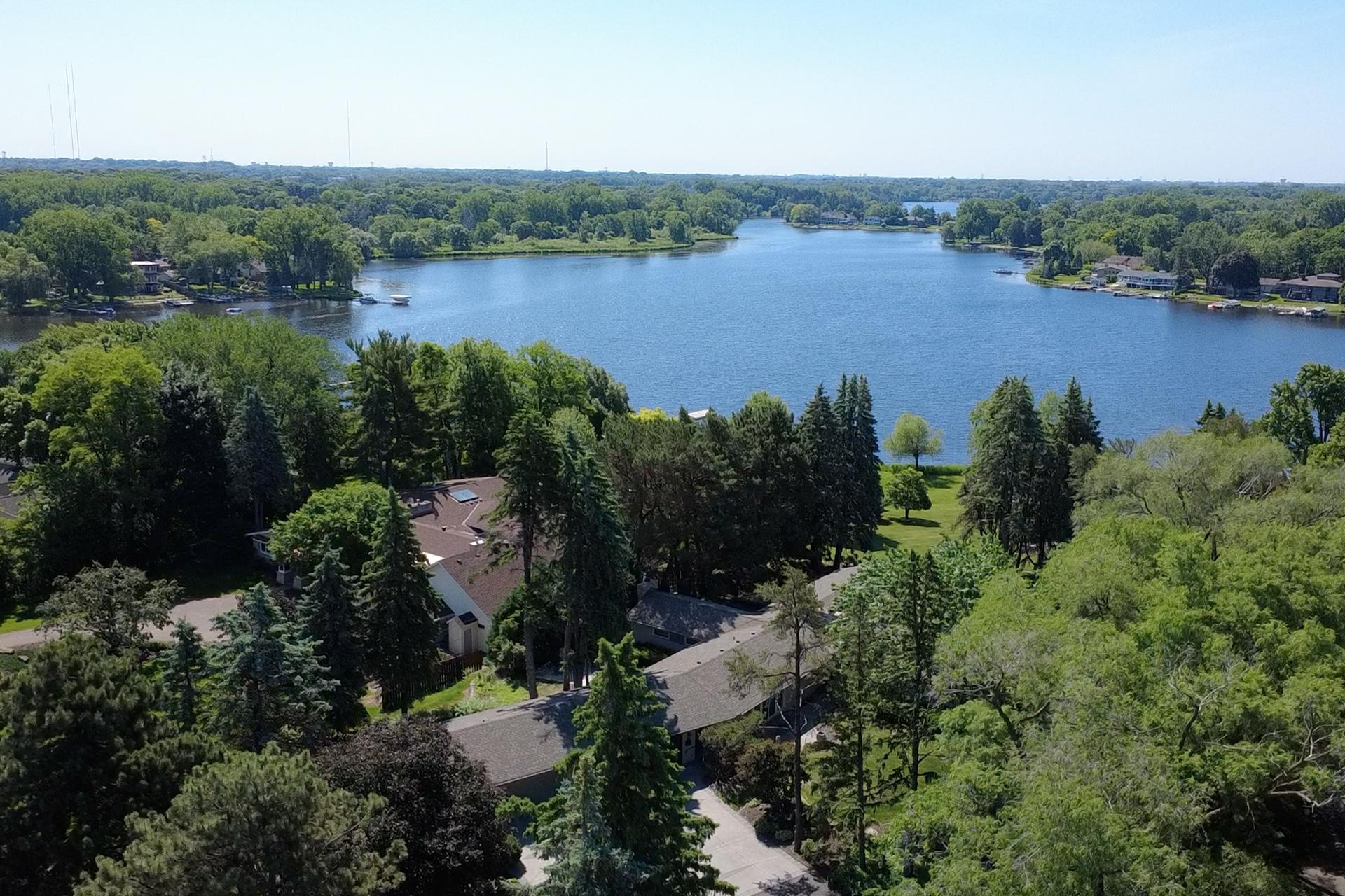 Aerial view of a lakeside neighborhood, with a tree-lined lake beyond homes in the foreground.
