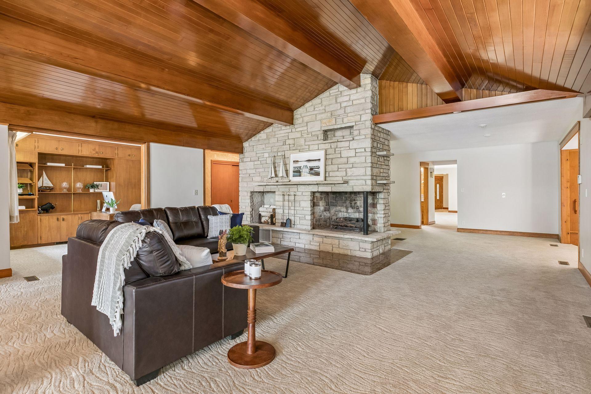 Living room with vaulted wood ceiling, stone fireplace, leather sofa, and built-in shelving.