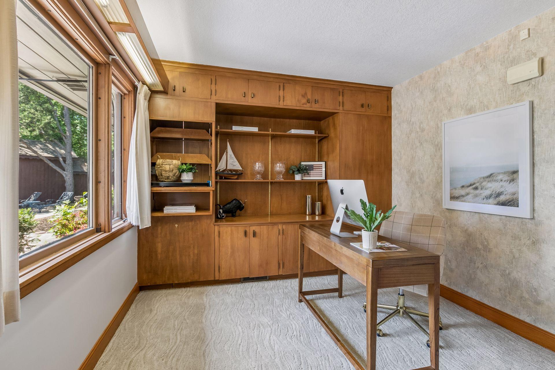 Home office with built-in wood cabinetry, a desk and computer beside a large window.