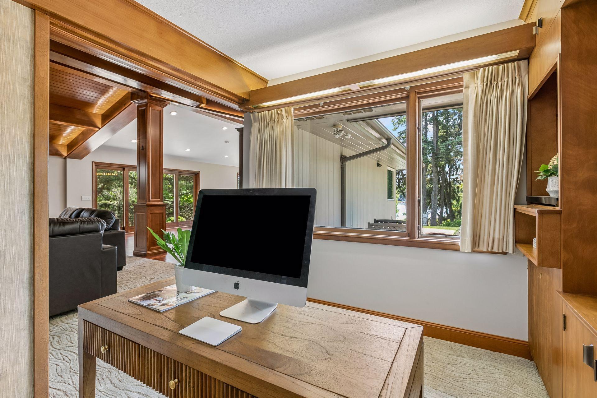 Home office with a wooden desk, built-in cabinetry, and a large window overlooking trees.