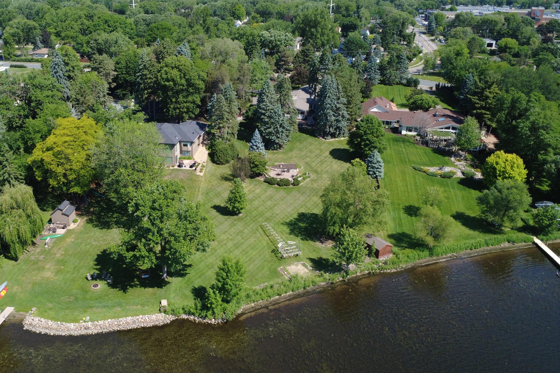 Aerial view of a lakeside property with expansive lawns, mature trees, and a rocky shoreline.