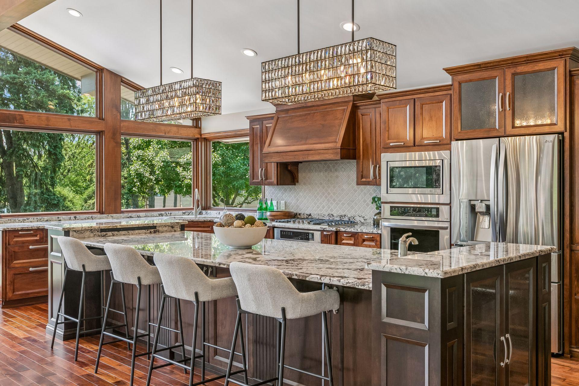 Kitchen with a large granite island, dark wood cabinetry, stainless steel appliances, and broad windows.