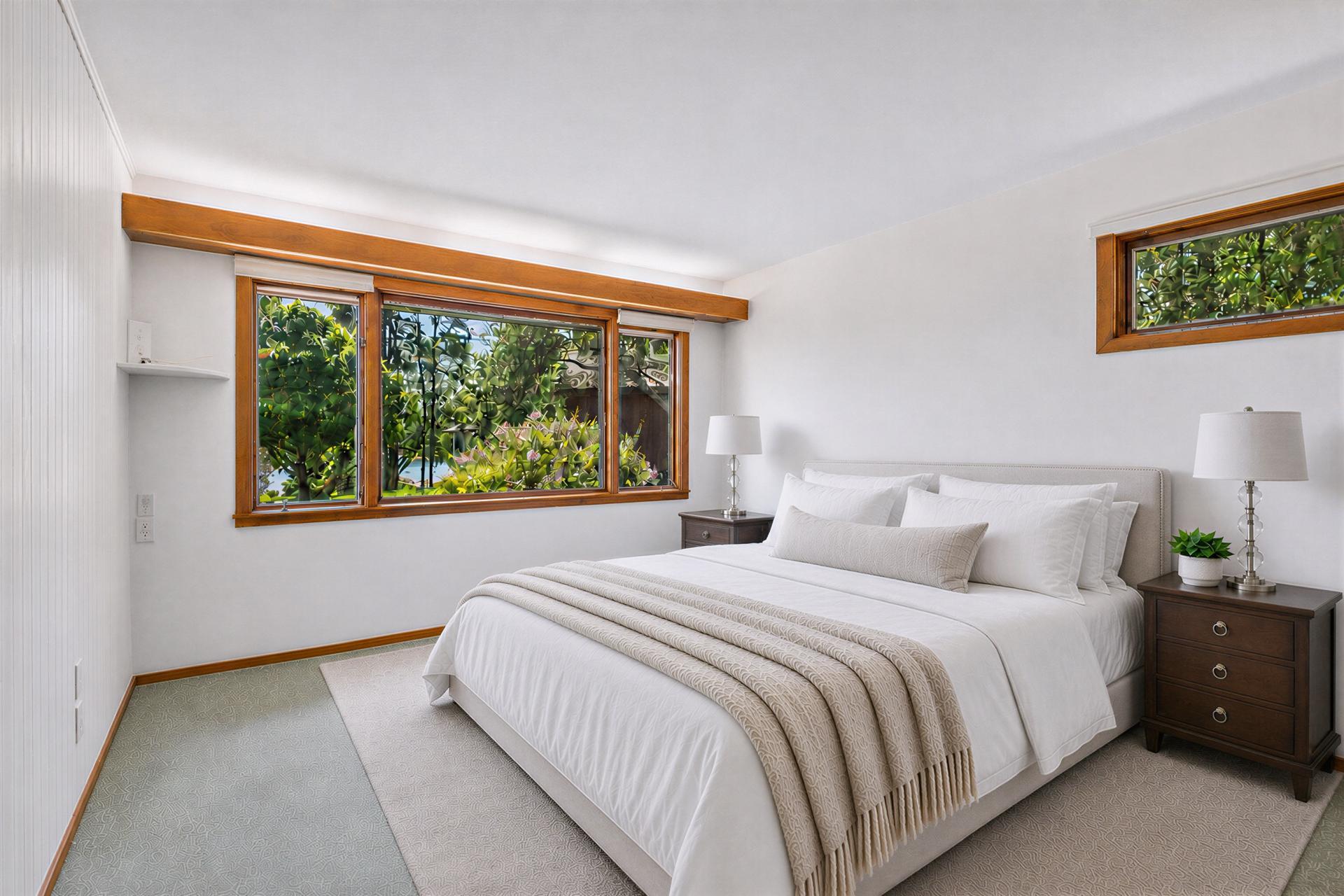 Bedroom with a white bed and wide wood-trimmed windows overlooking greenery
