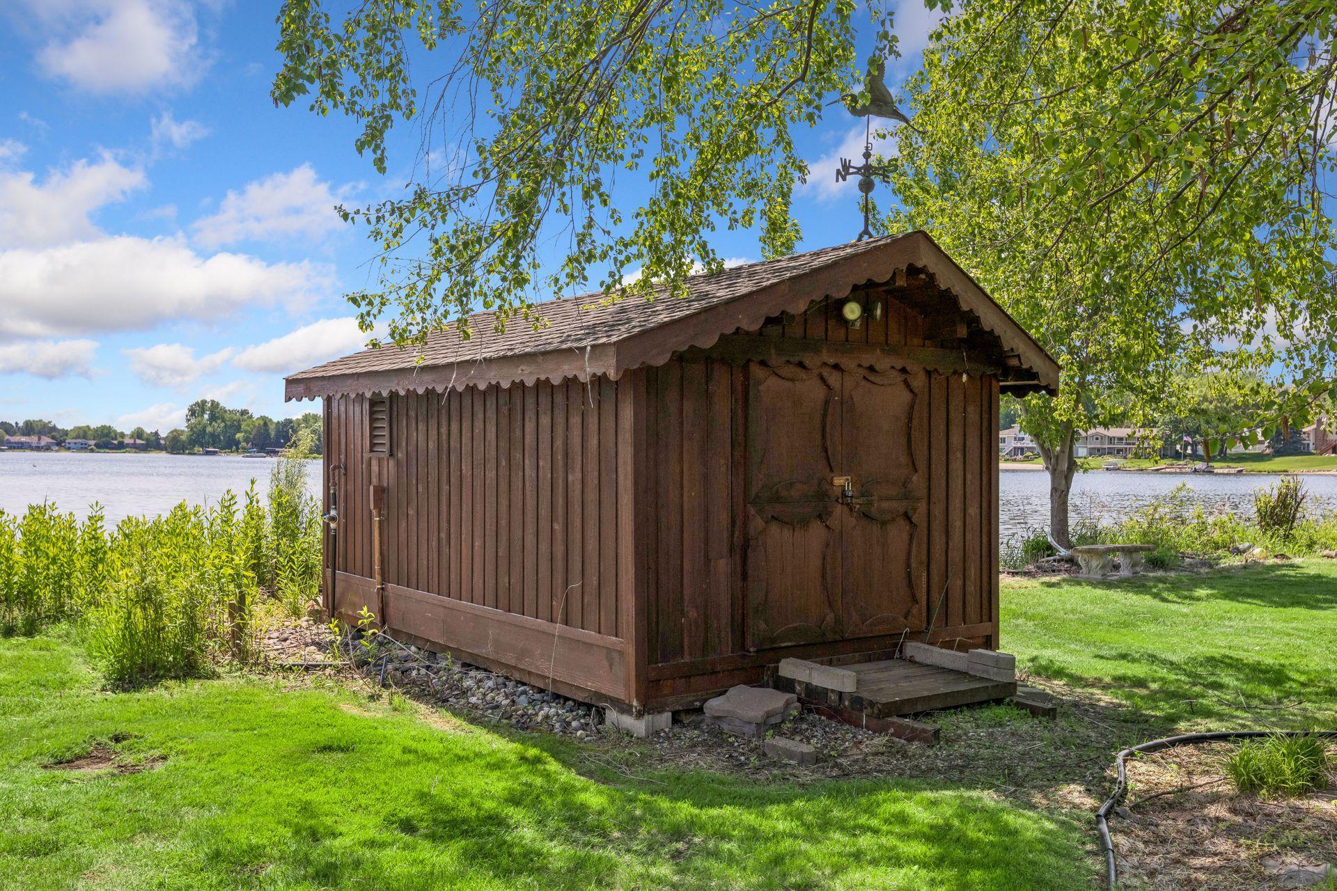 Wooden shed beside the lake, framed by trees and lawn.
