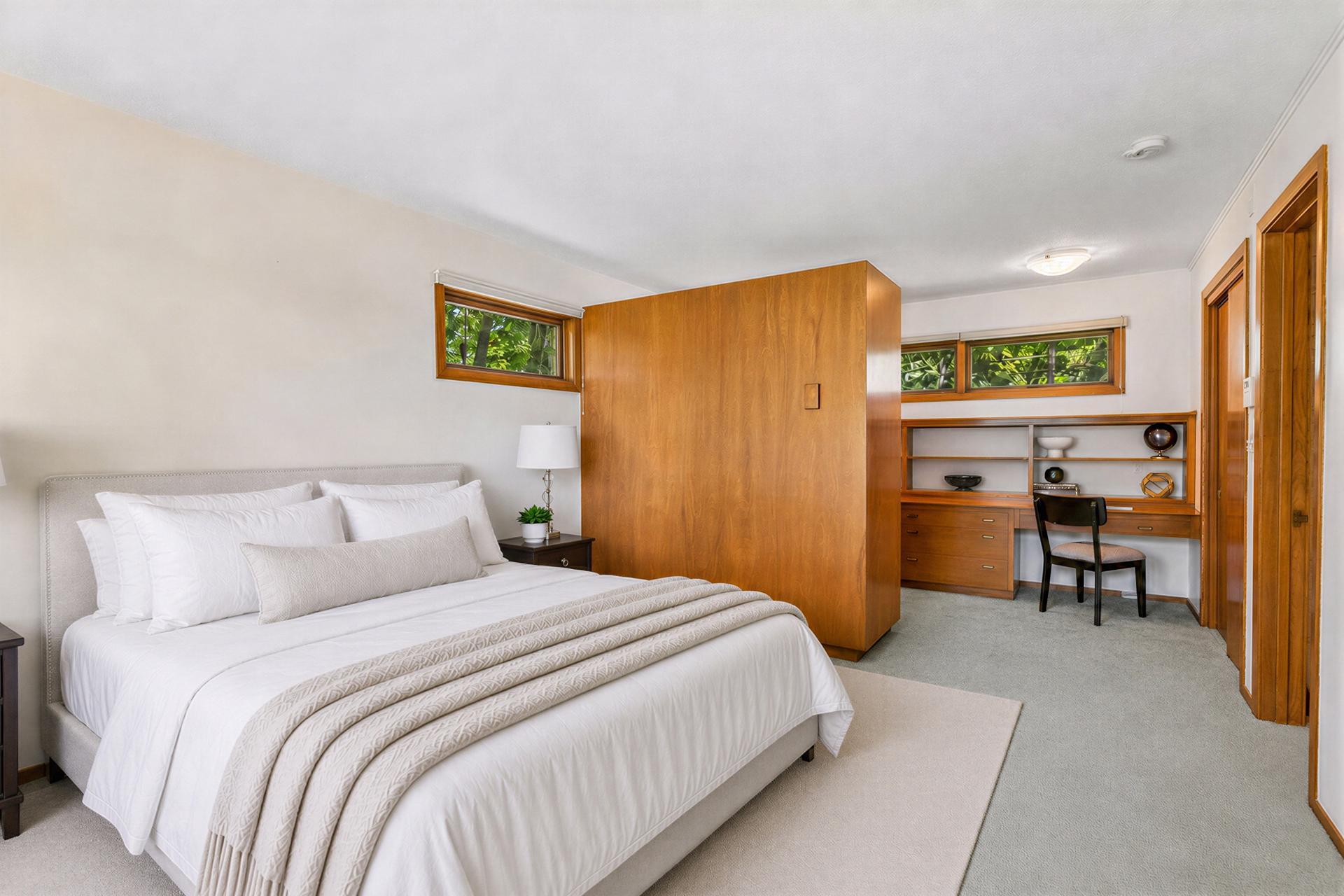 Bedroom with a large bed, warm wood partition, and built-in desk and shelving.