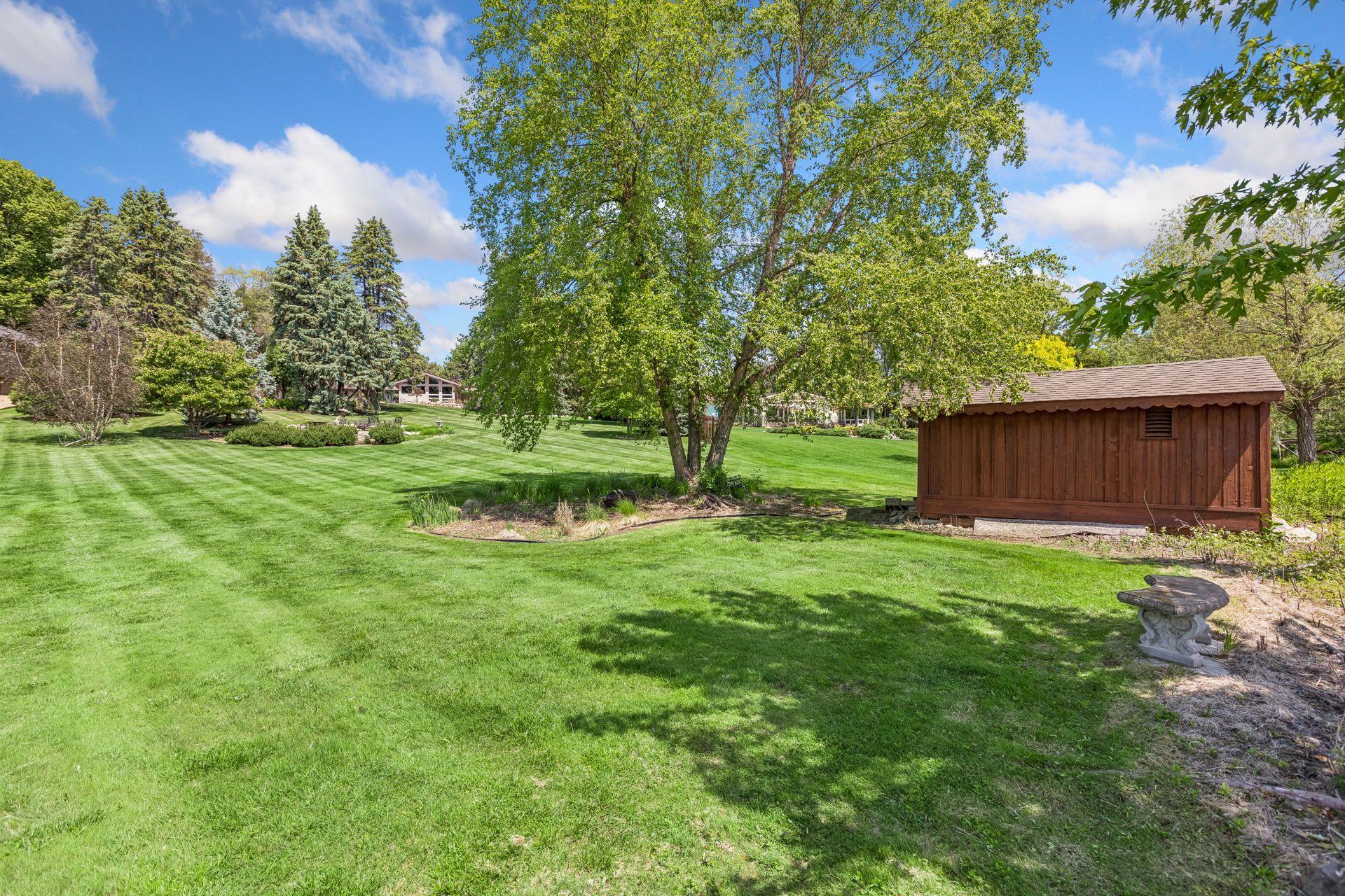 Expansive green lawn with mature trees, garden beds, and a wooden shed.