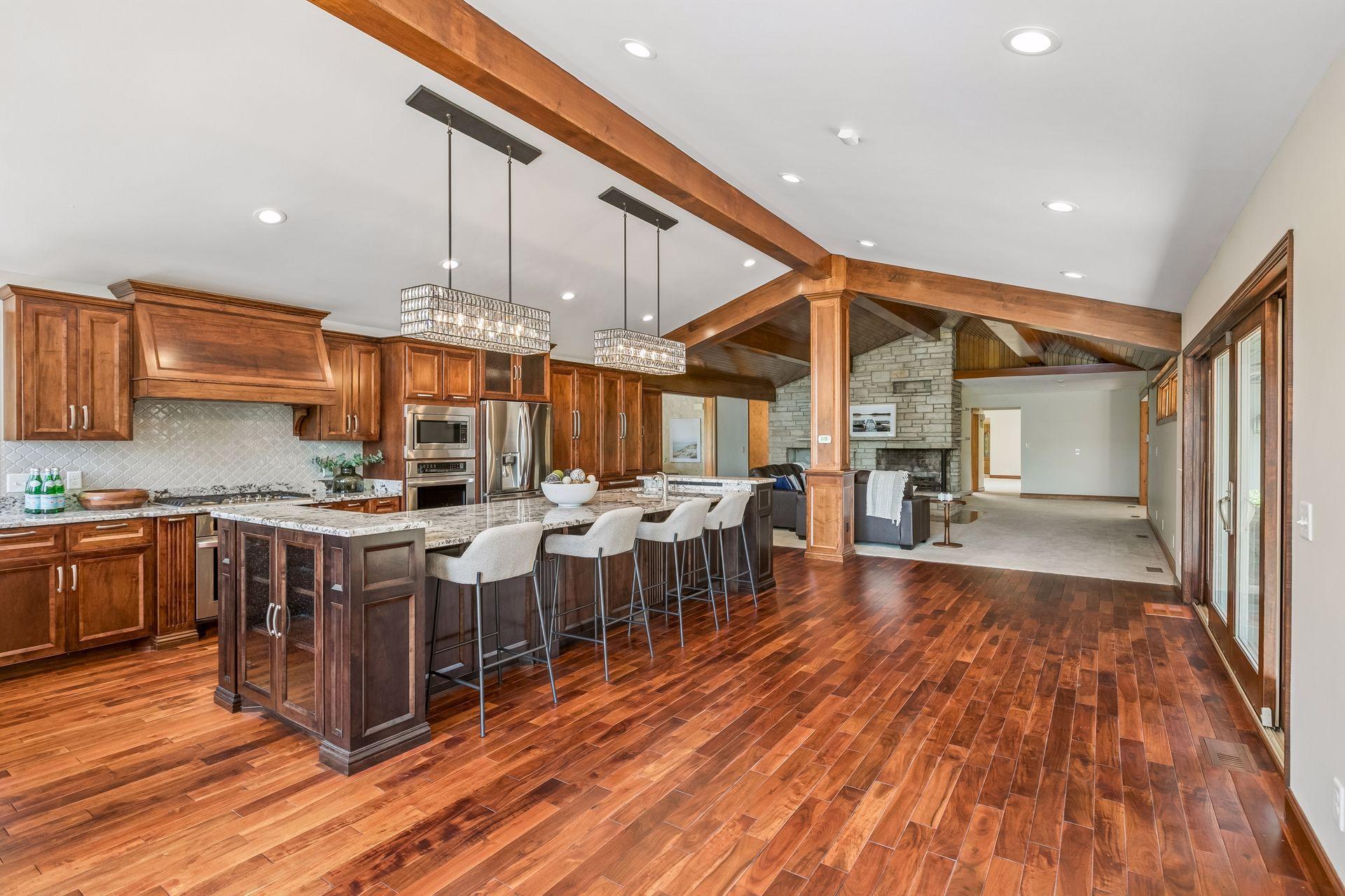 Open-plan kitchen with a granite island, rich wood cabinetry, exposed beams, and a stone fireplace.
