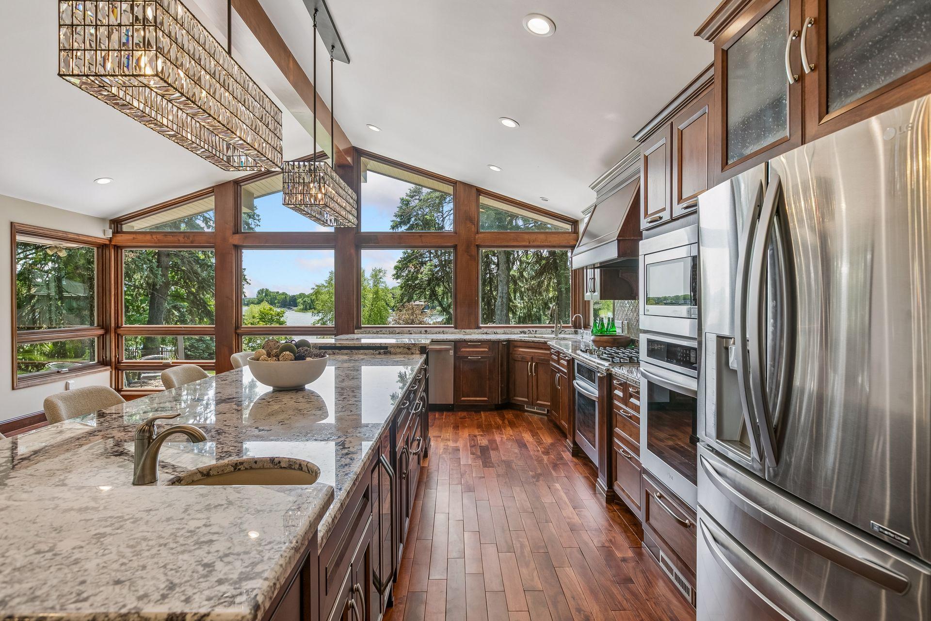 Kitchen with granite island, dark wood cabinetry, stainless steel appliances, and tall windows overlooking a lake.