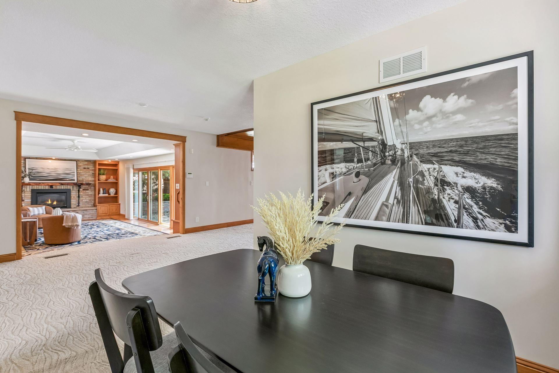 Dining area with a large sailboat photograph and an open view into a living room with a brick fireplace.