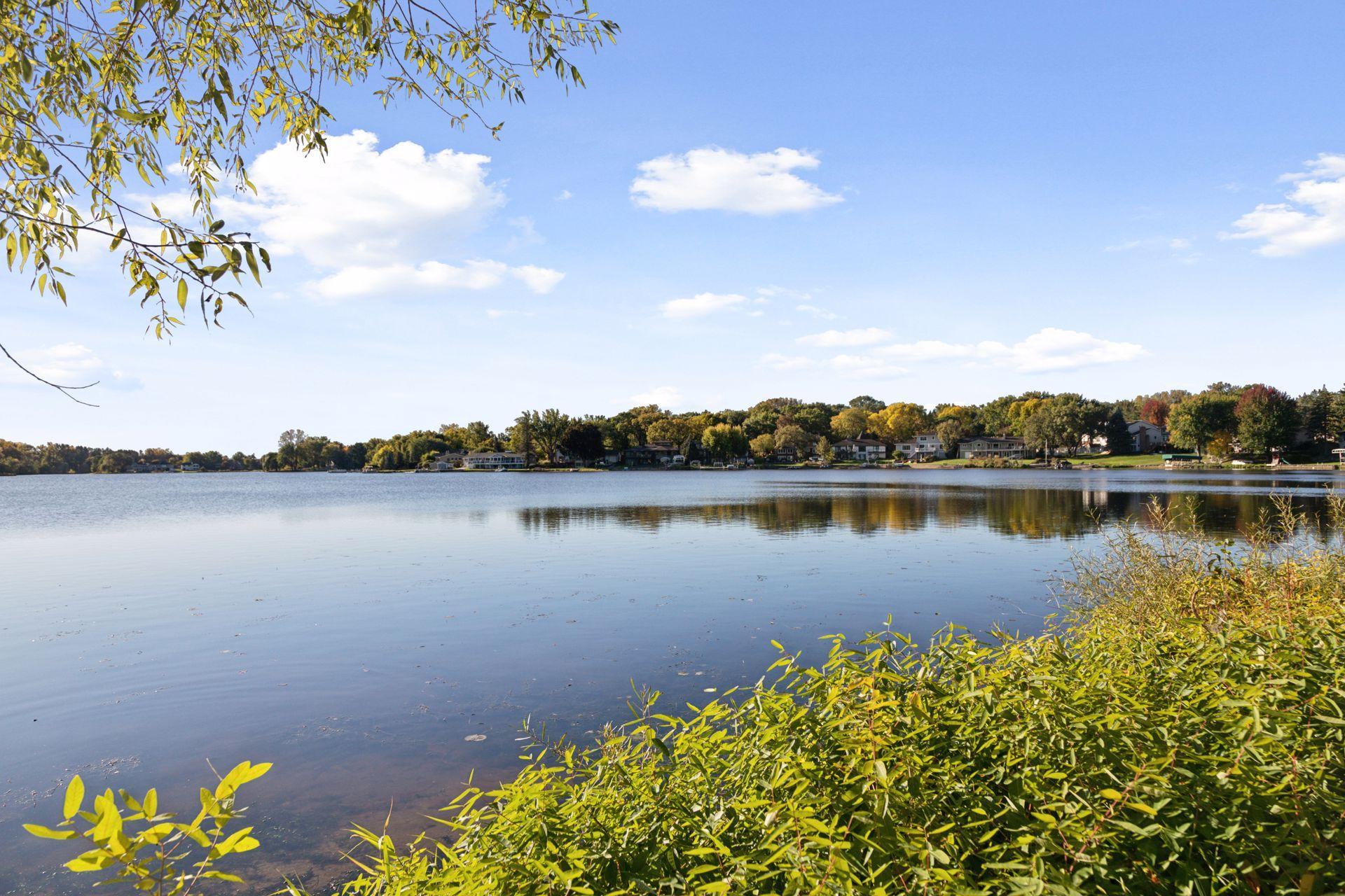 Lake view across calm water to a tree-lined shore with homes and autumn foliage.
