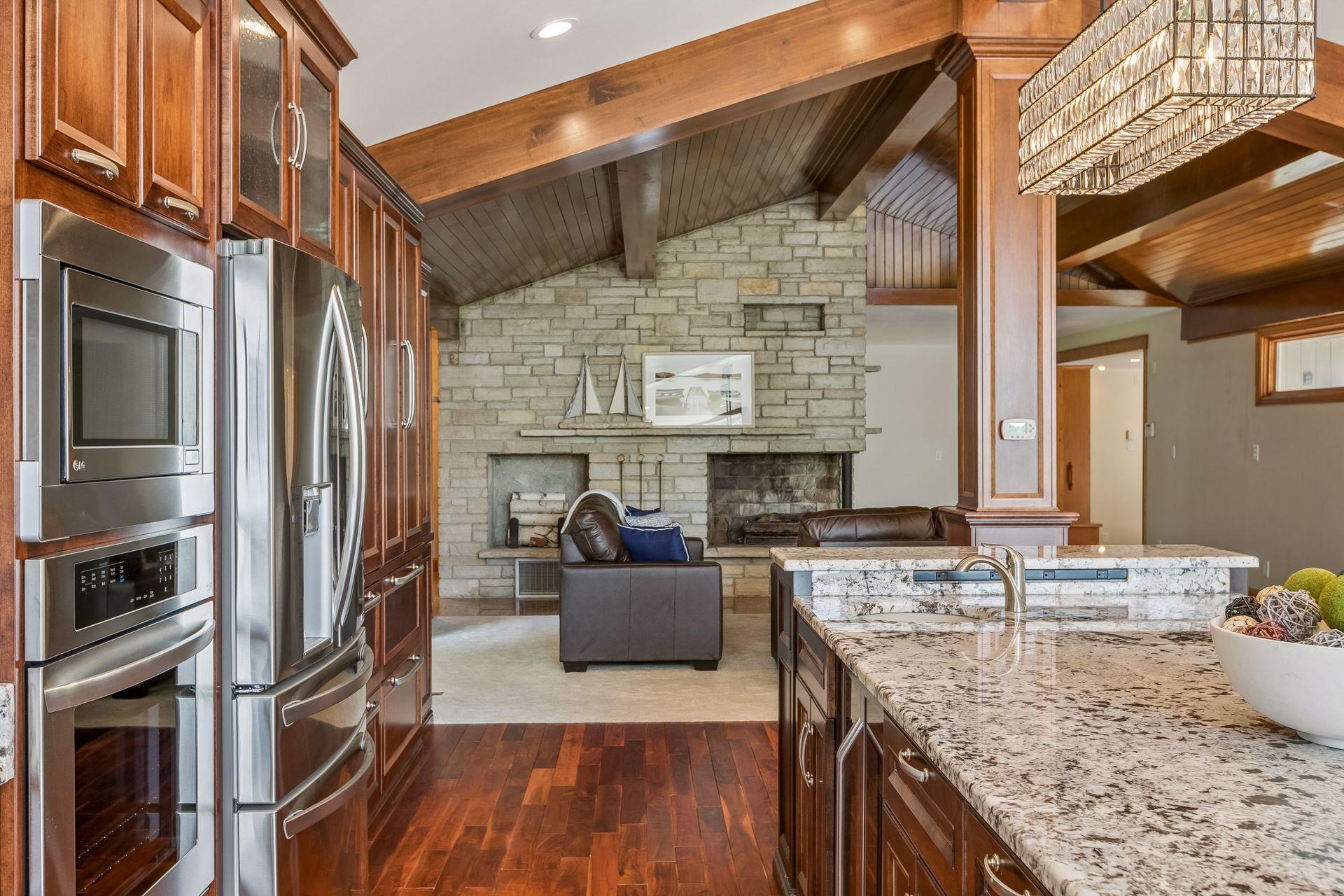 Kitchen with granite island, stainless appliances, and stone fireplace beneath a vaulted wood ceiling.