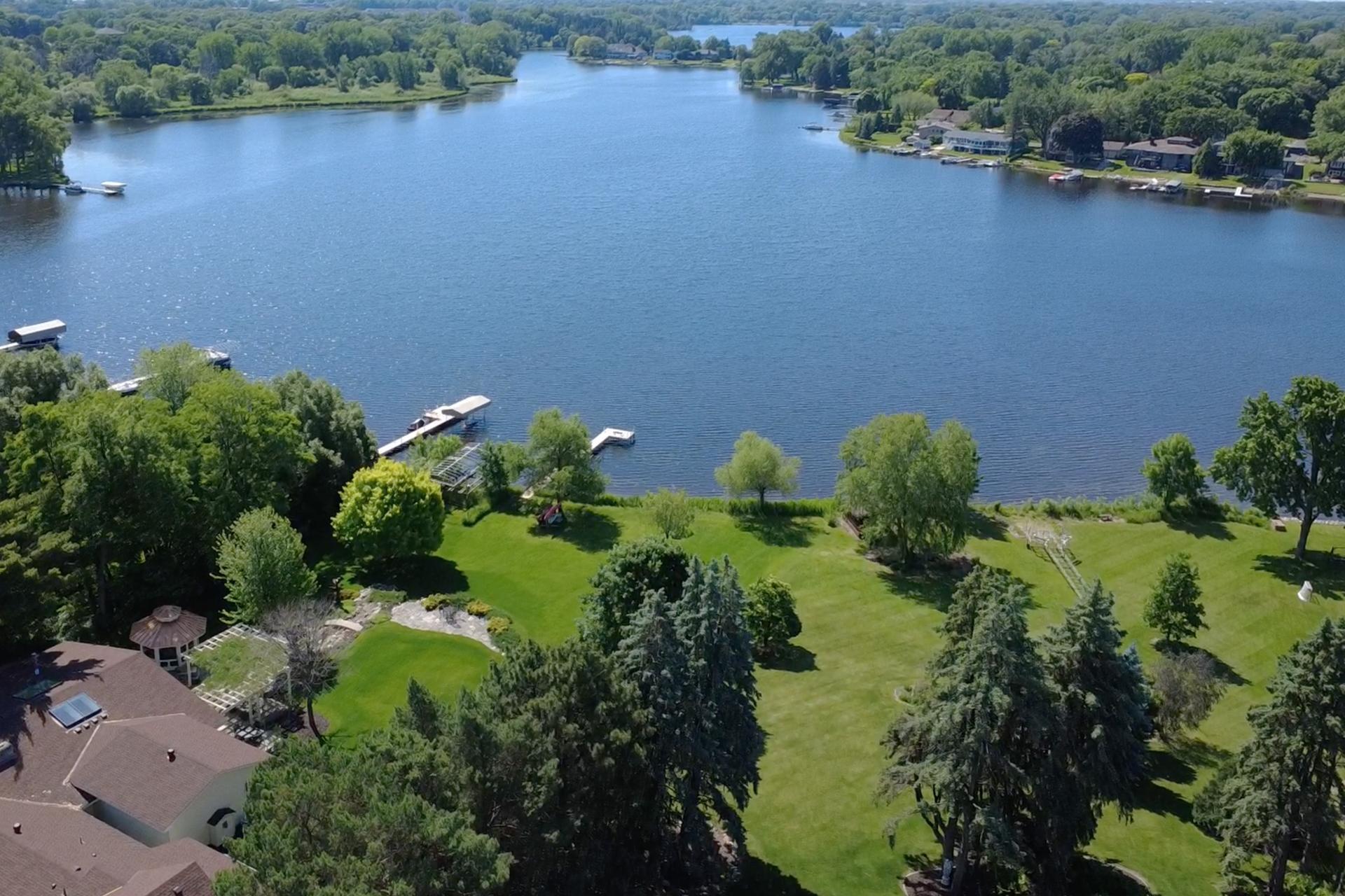 Aerial view of a lakeside property with a large lawn, mature trees, and docks along the water.